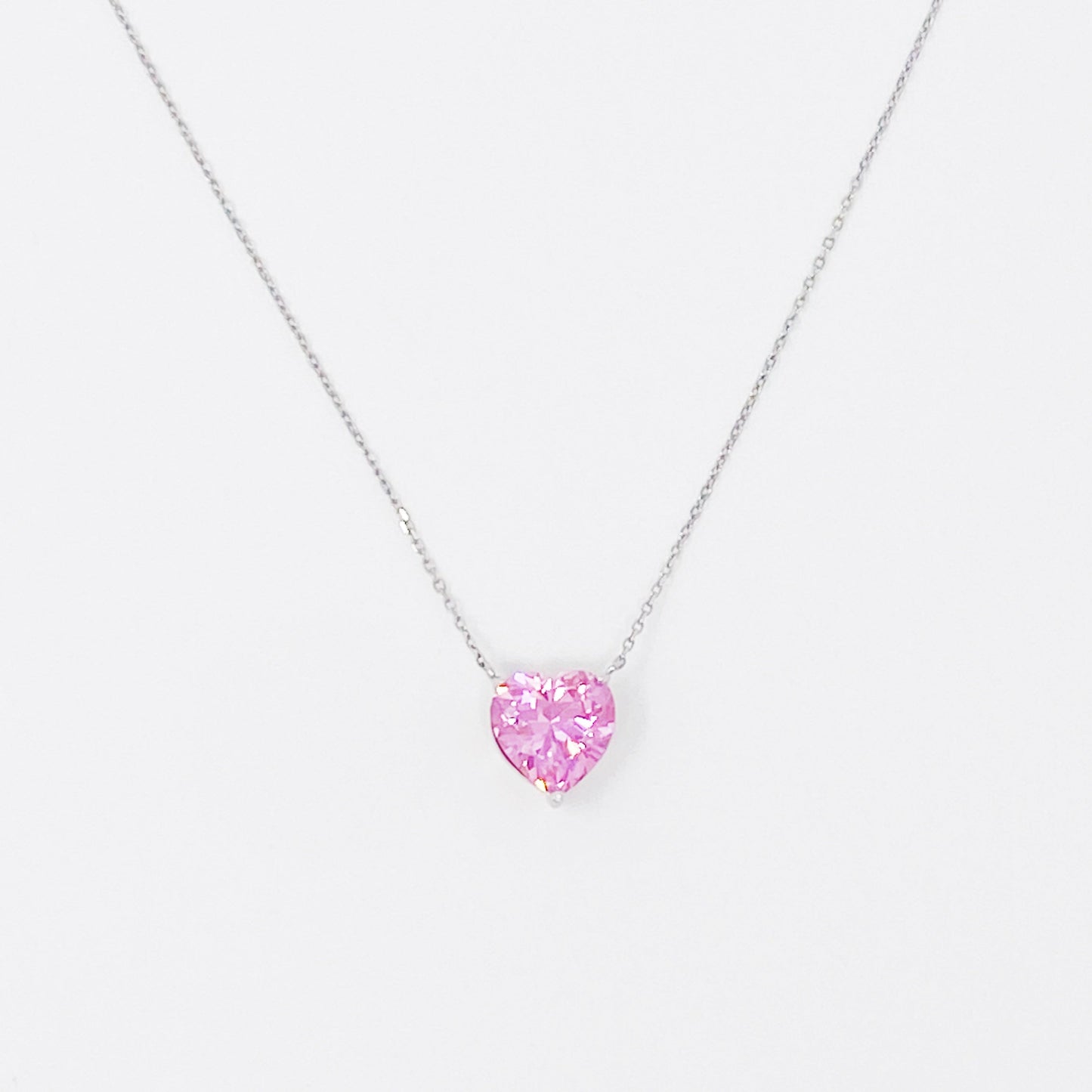Two Absolute Beauty sterling silver heart necklaces by Ellison + Young; one with a pink gem, the other with a clear gem, against a white background.
