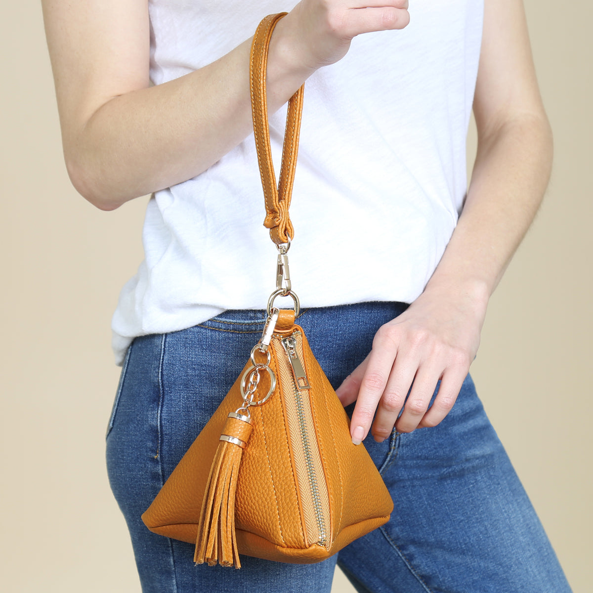 A person in a white shirt and jeans is holding the Riah Fashion Pyramid Shape Tassel Wristlet Leather Bag in orange.