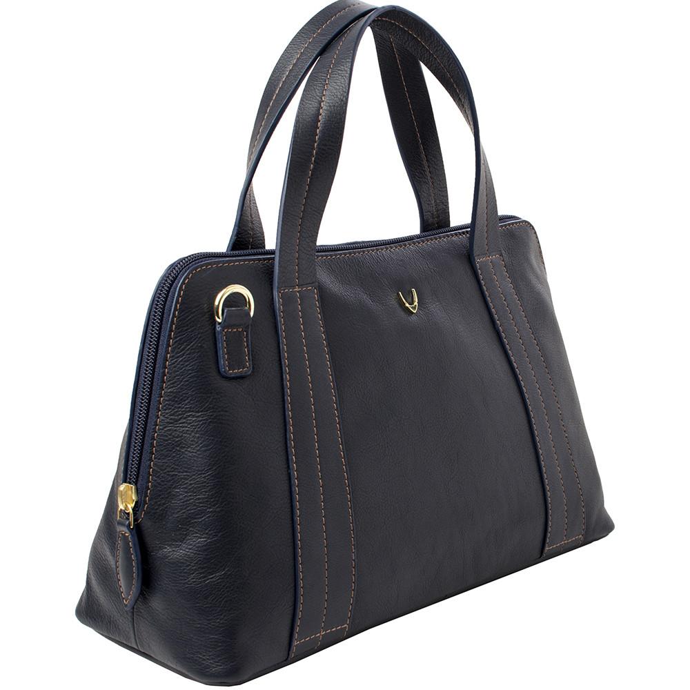 The Cerys Medium Leather Satchel by Hidesign is a red handbag with short handles and a detachable shoulder strap, featuring gold-tone hardware and a small gold emblem on the front.
