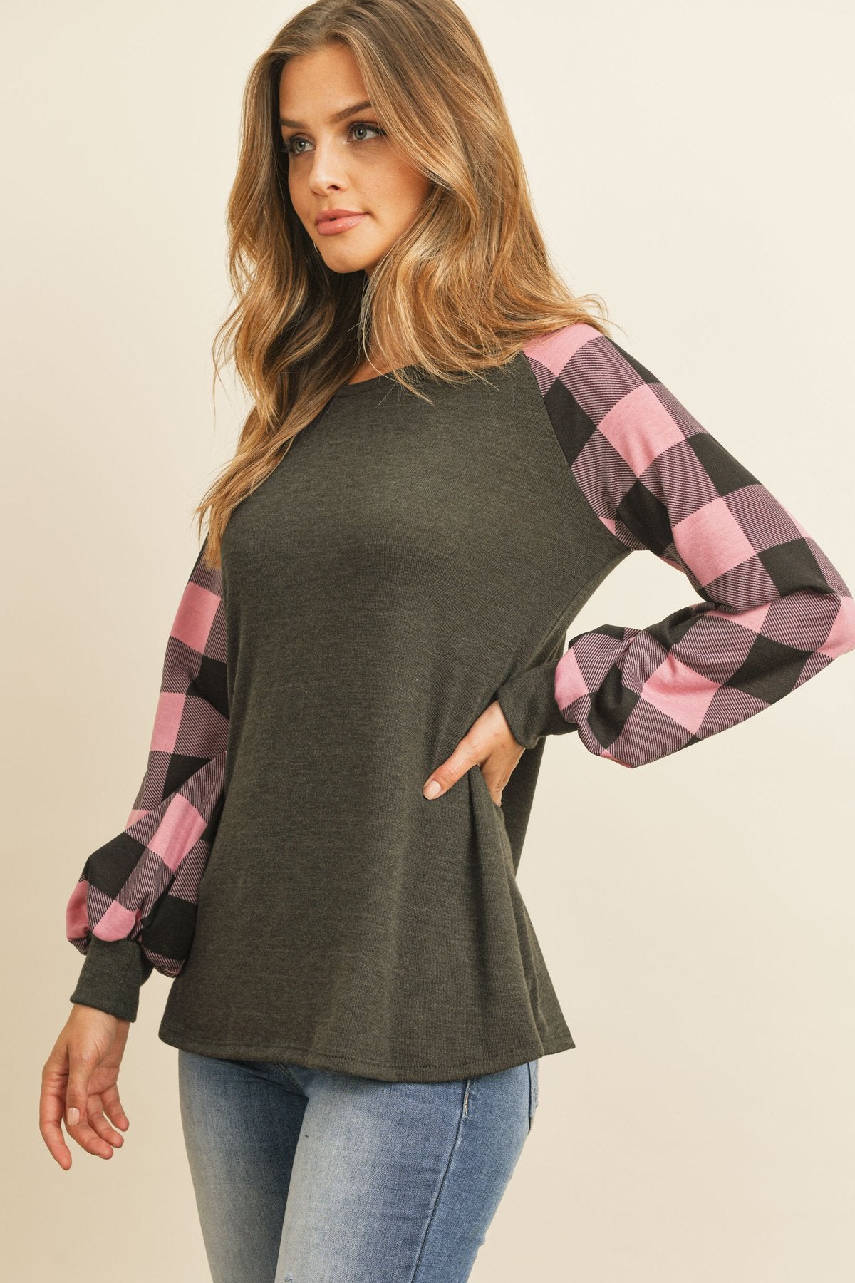 A woman wearing a faded denim plaid puff sleeved round neck top by Riah Fashion and ripped jeans stands against a plain background.