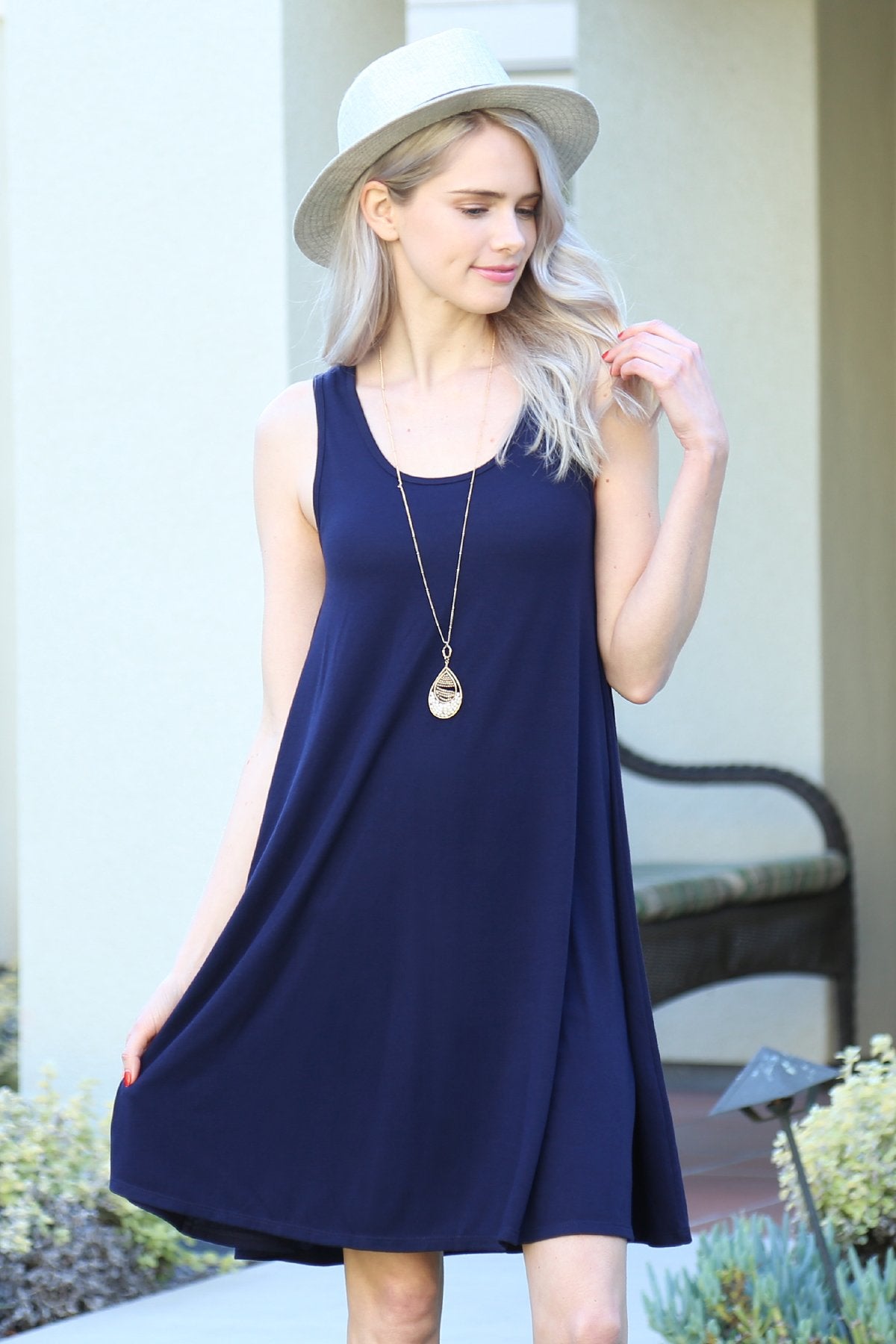 A person with long, light-colored hair wears a Sleeveless Flared Pocket Dress in light green by Riah Fashion outside, holding the dresss sides along with a triangular pendant necklace.