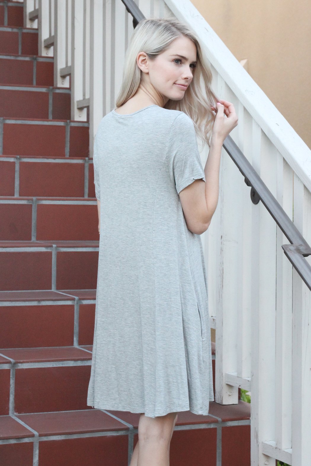 A person with long hair wearing a rust-colored Short Sleeve Strappy Pocket Dress by Riah Fashion stands on a staircase, holding the side of the dress with one hand.