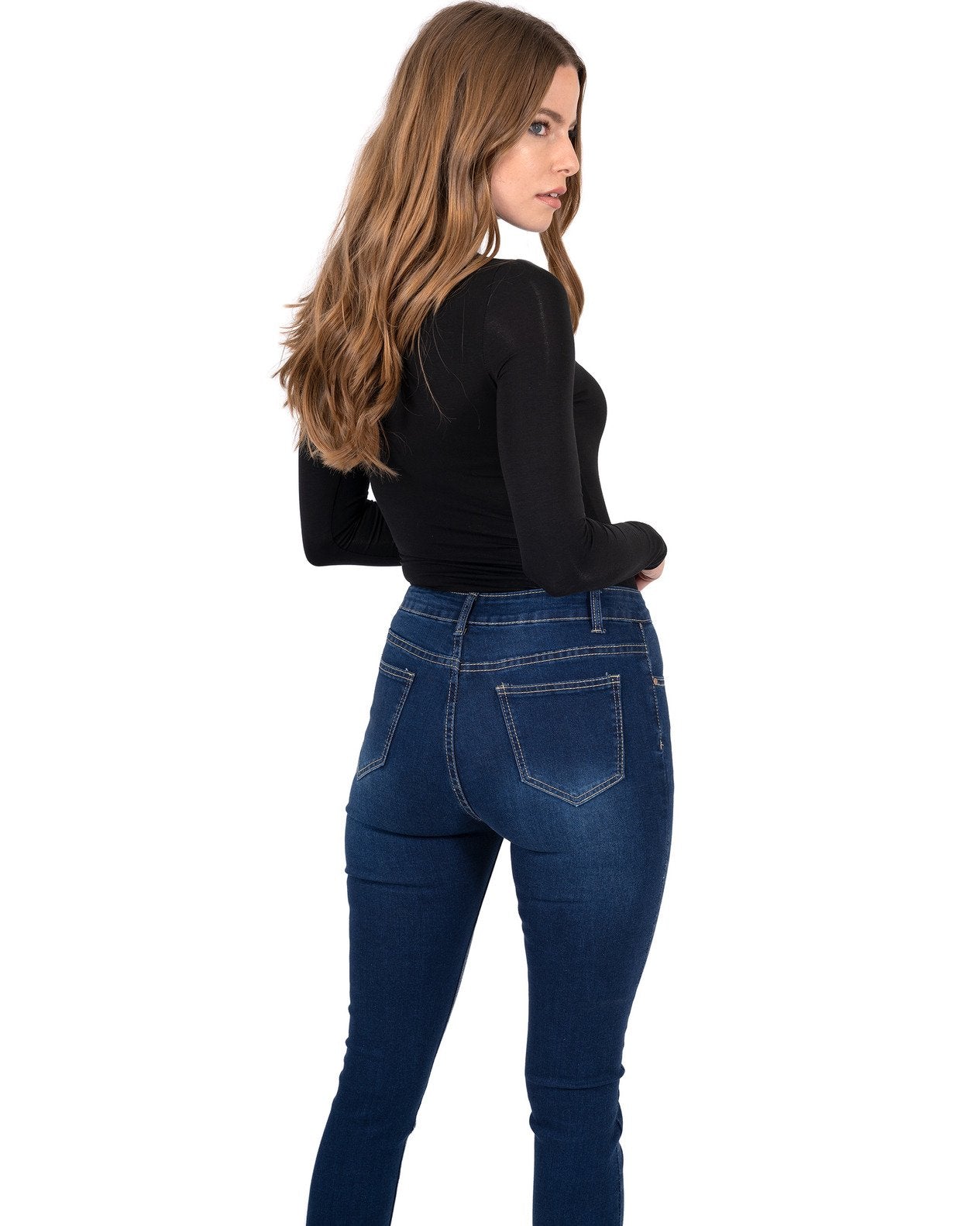 A person stands by a pool wearing a black long-sleeve shirt, Alexis High Waist Skinny Jeans by Savoy Active, and heels. Tall trees and vibrant flowers surround the area.