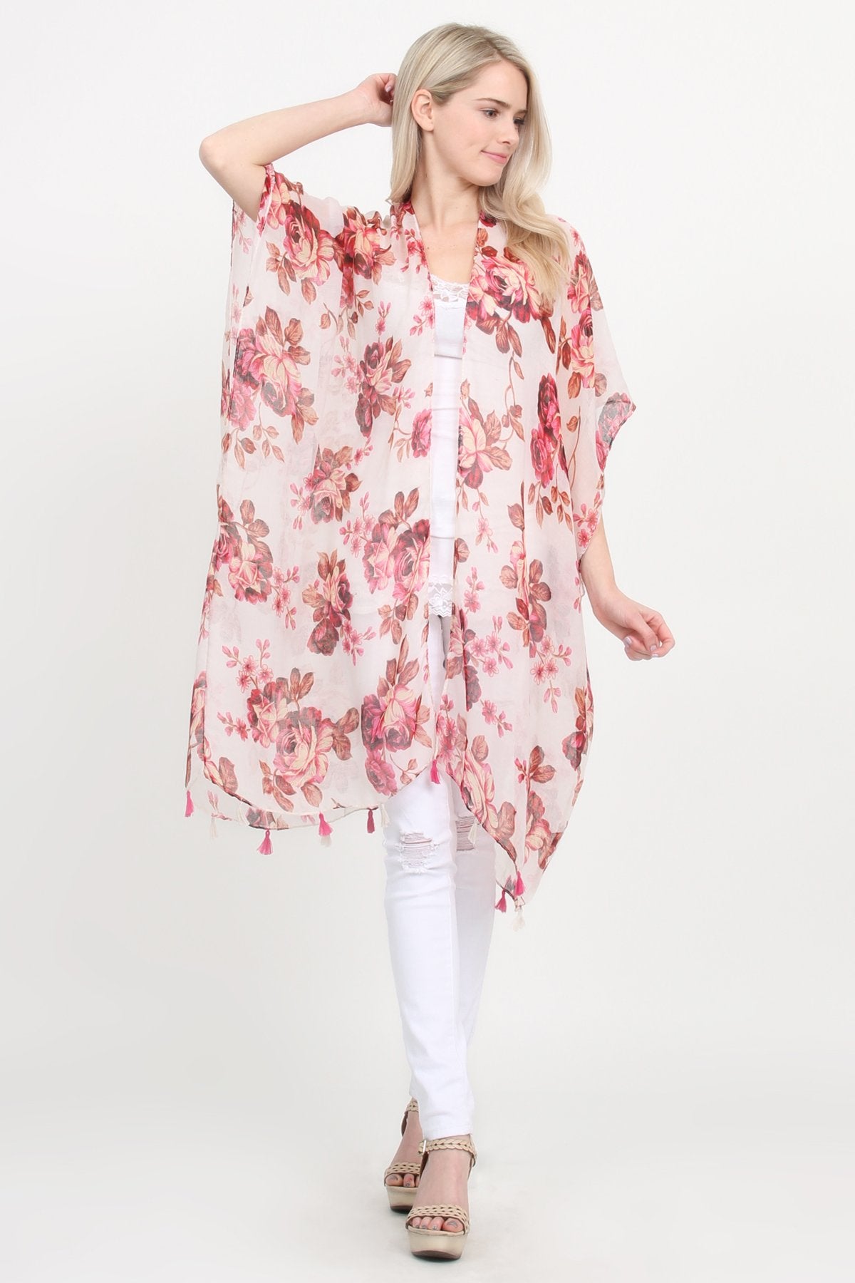 A woman stands against a plain background, wearing a Riah Fashion beige blue open front knee-length floral cardigan over a white outfit.
