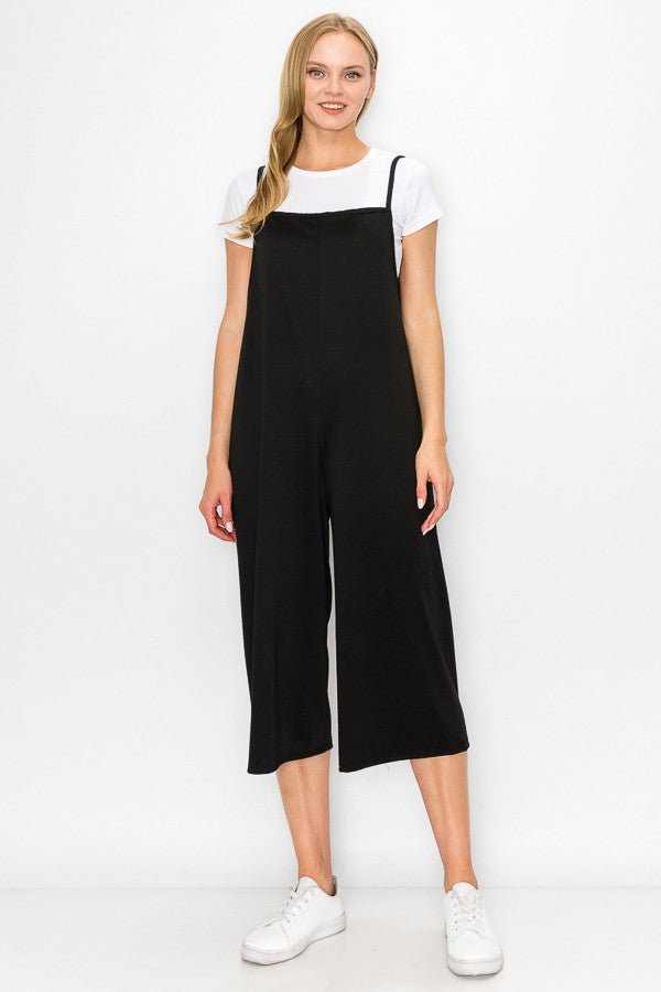 A person models the Stylespect Cropped Bottom Wide Leg Oversized Jumpsuit in black, paired with a white t-shirt and white sneakers, set against a plain white backdrop.