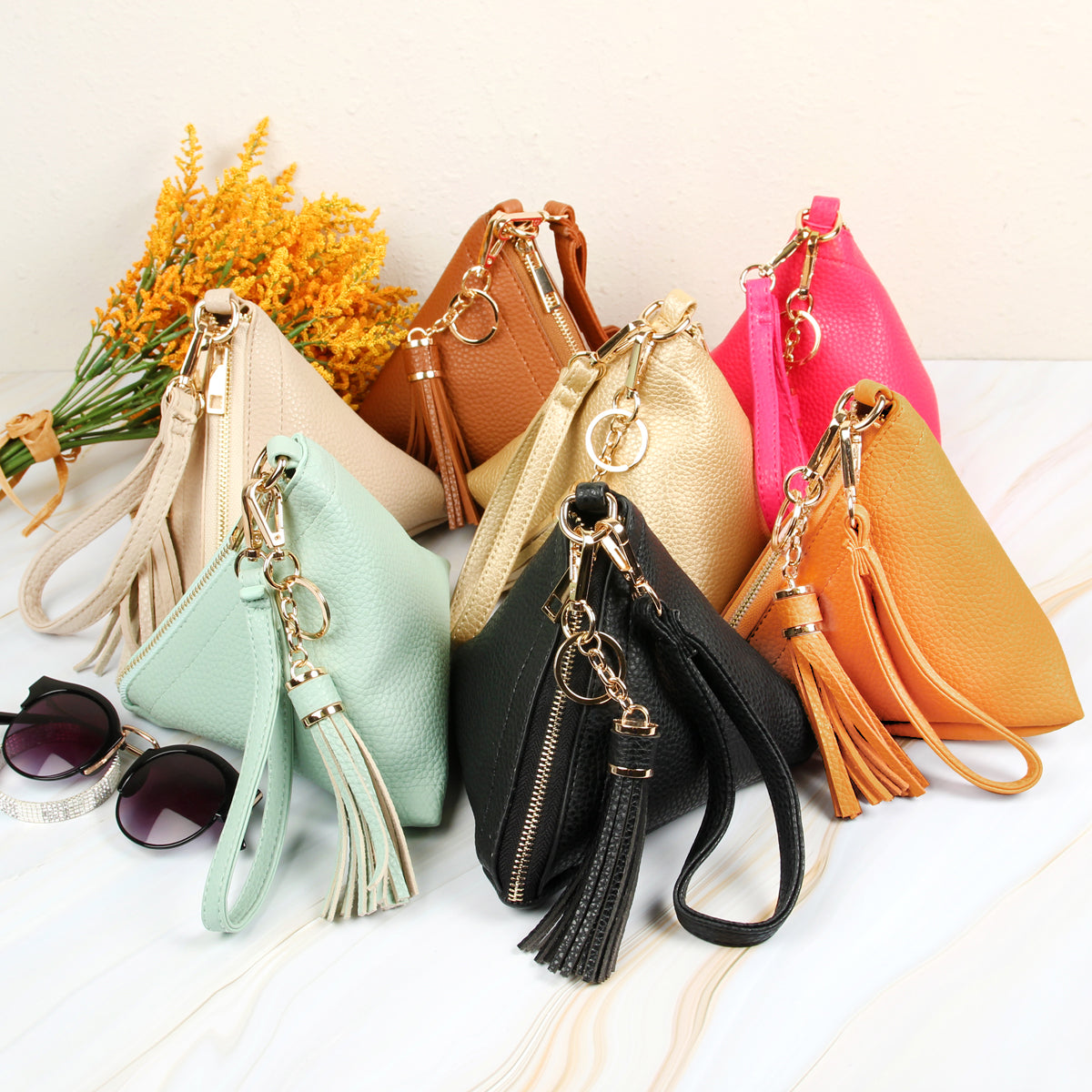 A person in a white shirt and jeans is holding the Riah Fashion Pyramid Shape Tassel Wristlet Leather Bag in orange.