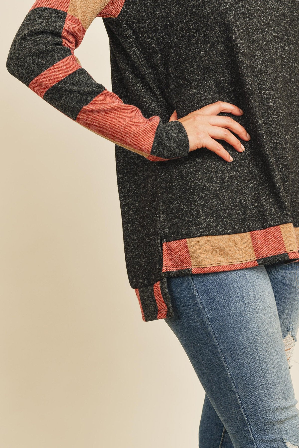 A woman in a Riah Fashion Brush Hacci Plaid Contrast Long Back Hem Top with red and beige accents, paired with blue ripped jeans, stands against a plain background.