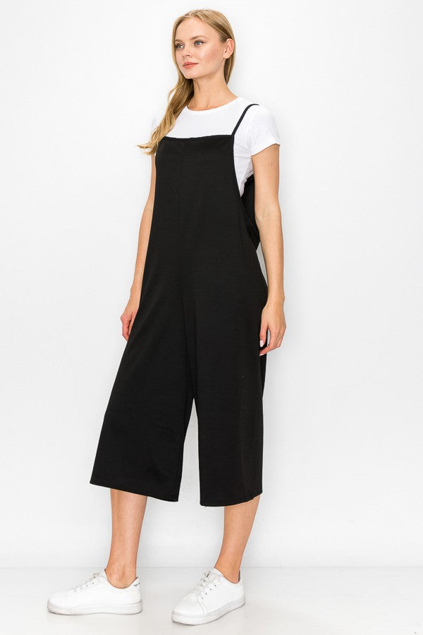 A person models the Stylespect Cropped Bottom Wide Leg Oversized Jumpsuit in black, paired with a white t-shirt and white sneakers, set against a plain white backdrop.