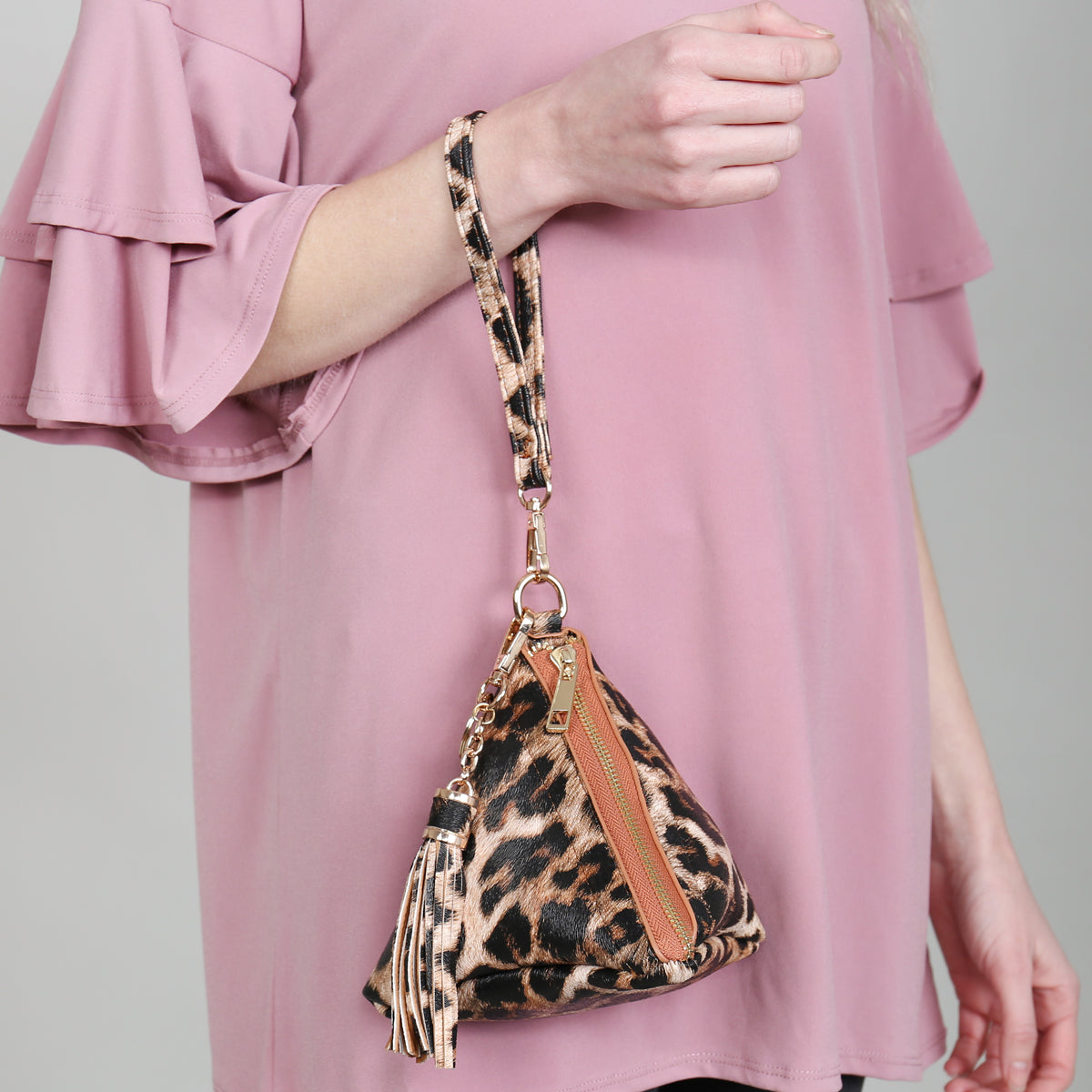A person in a white shirt and jeans is holding the Riah Fashion Pyramid Shape Tassel Wristlet Leather Bag in orange.