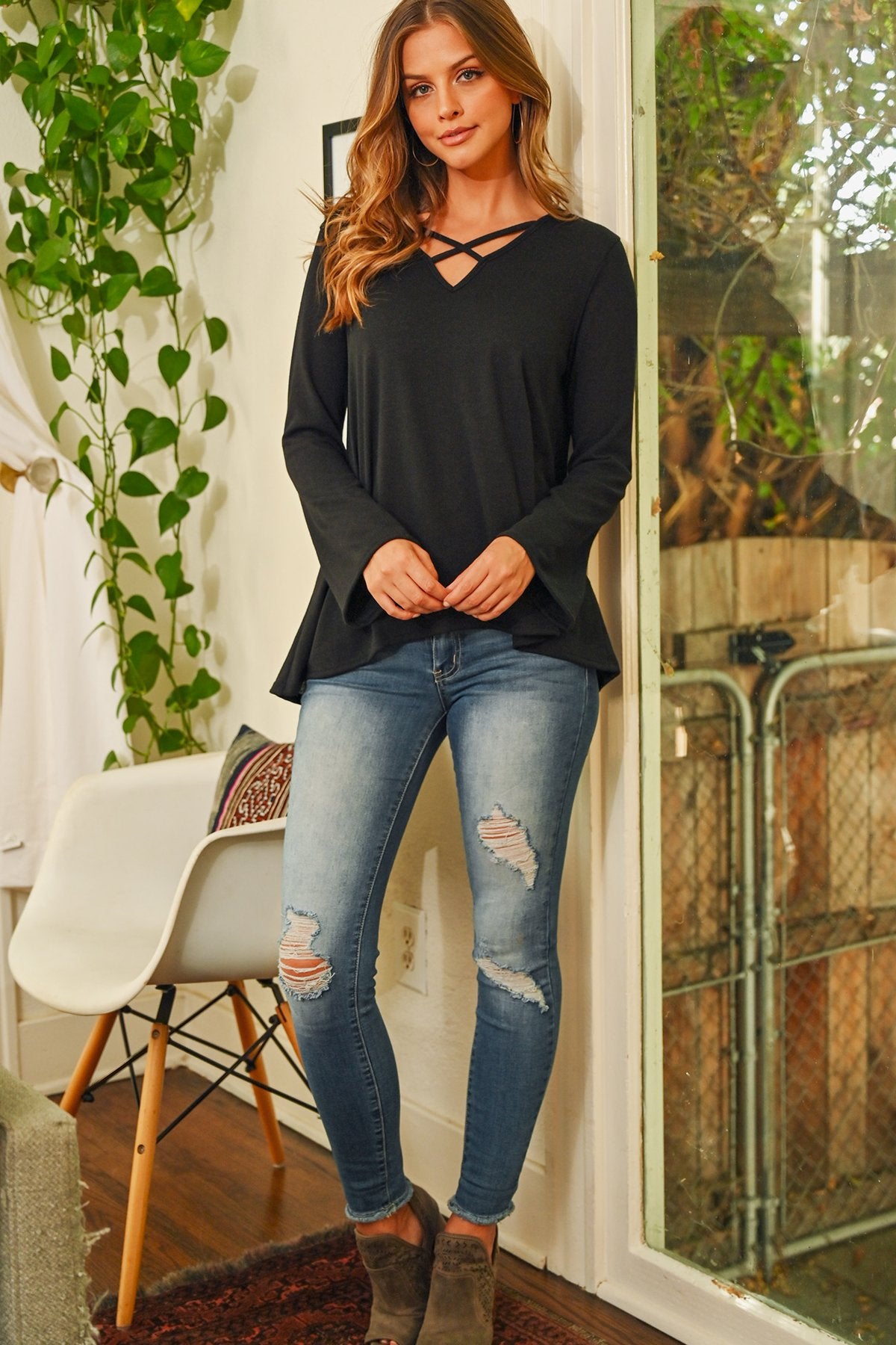 A person wearing a Riah Fashion Criss Cross Neck Long Sleeve Hacci Top in Dusty Blush and blue jeans stands against a neutral background, smiling.