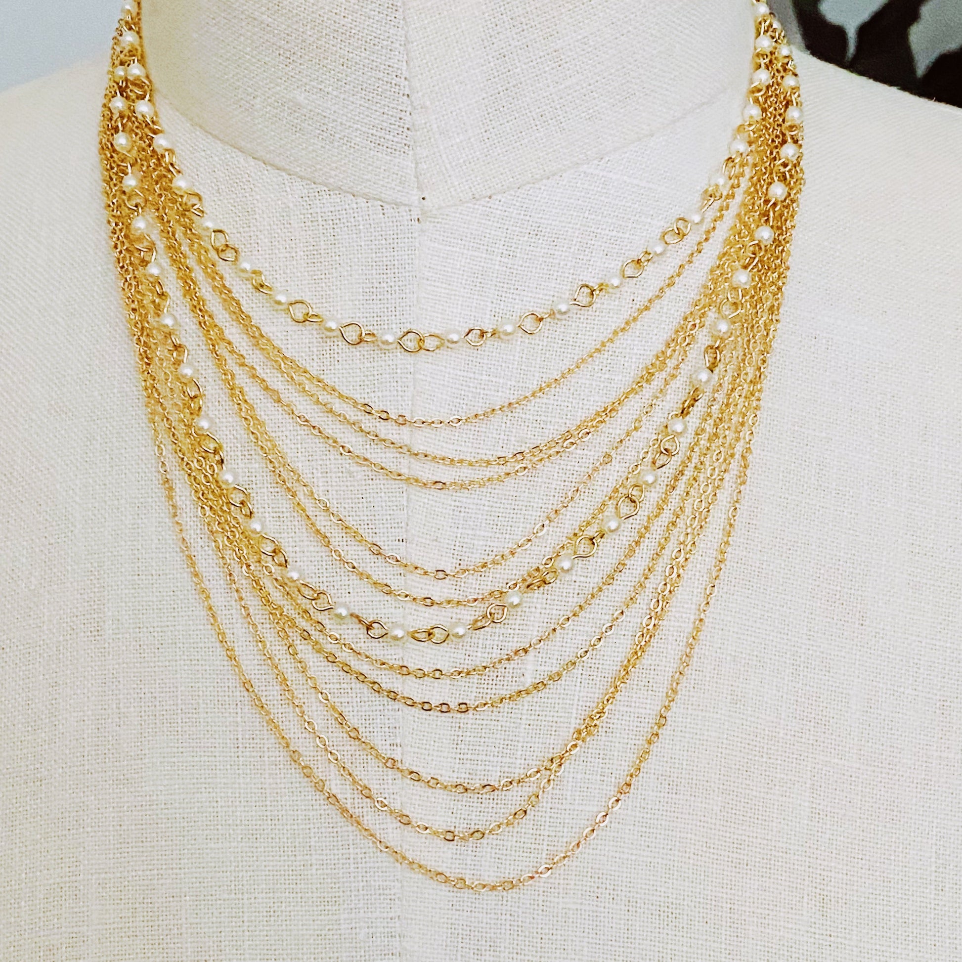 The Beautifully Draping Pearl and Chain Necklace by Ellison + Young is elegantly displayed on a white surface, showcasing its intricate chain designs.