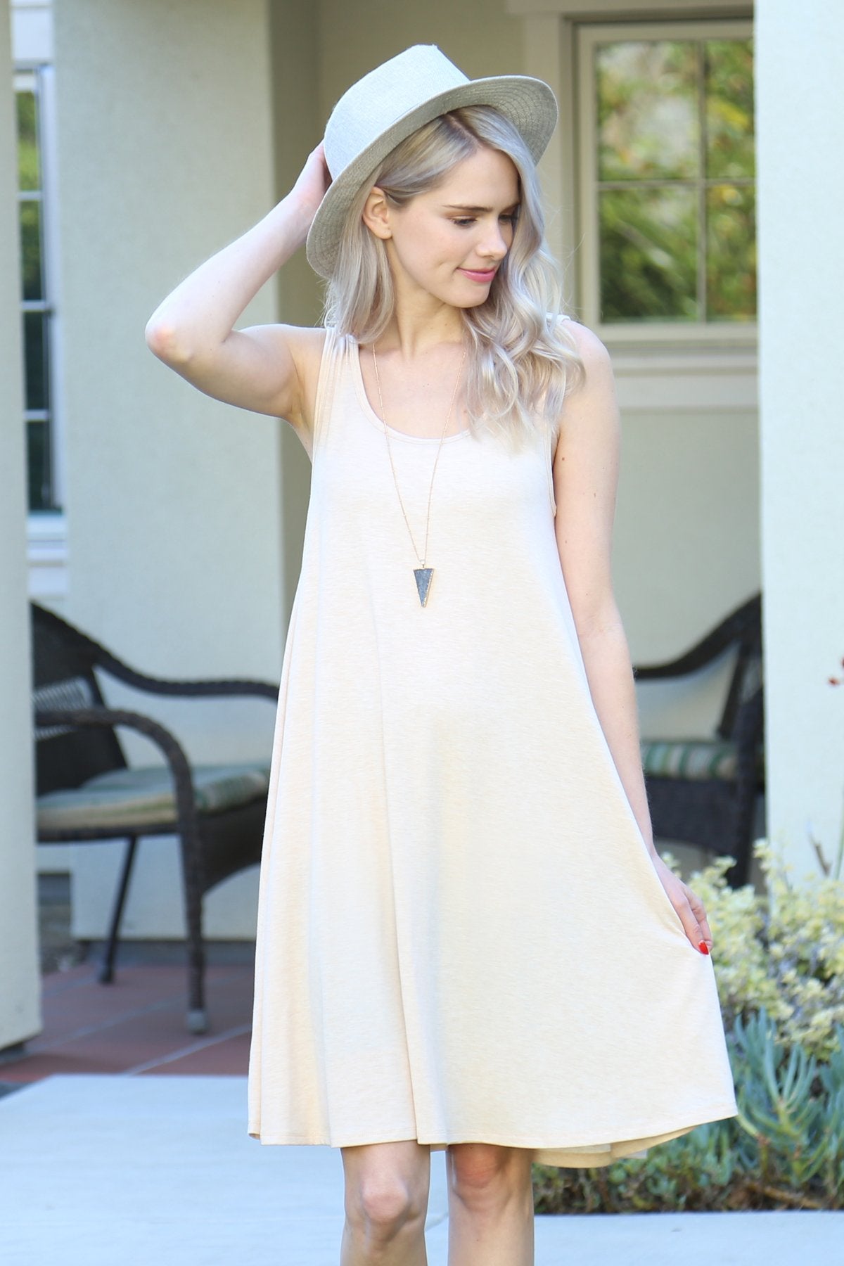A person with long, light-colored hair wears a Sleeveless Flared Pocket Dress in light green by Riah Fashion outside, holding the dresss sides along with a triangular pendant necklace.