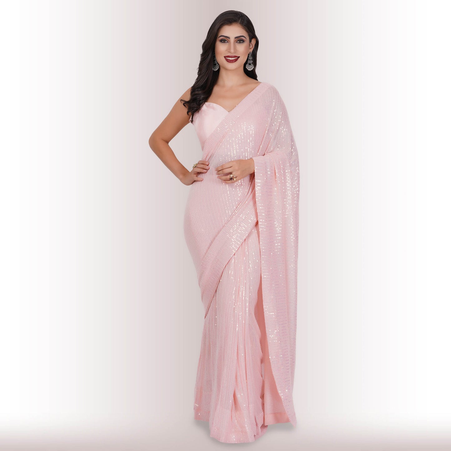 A person wearing Chiros Ready Made Sequin Saree in Blush poses with one hand on their hip against a light background.