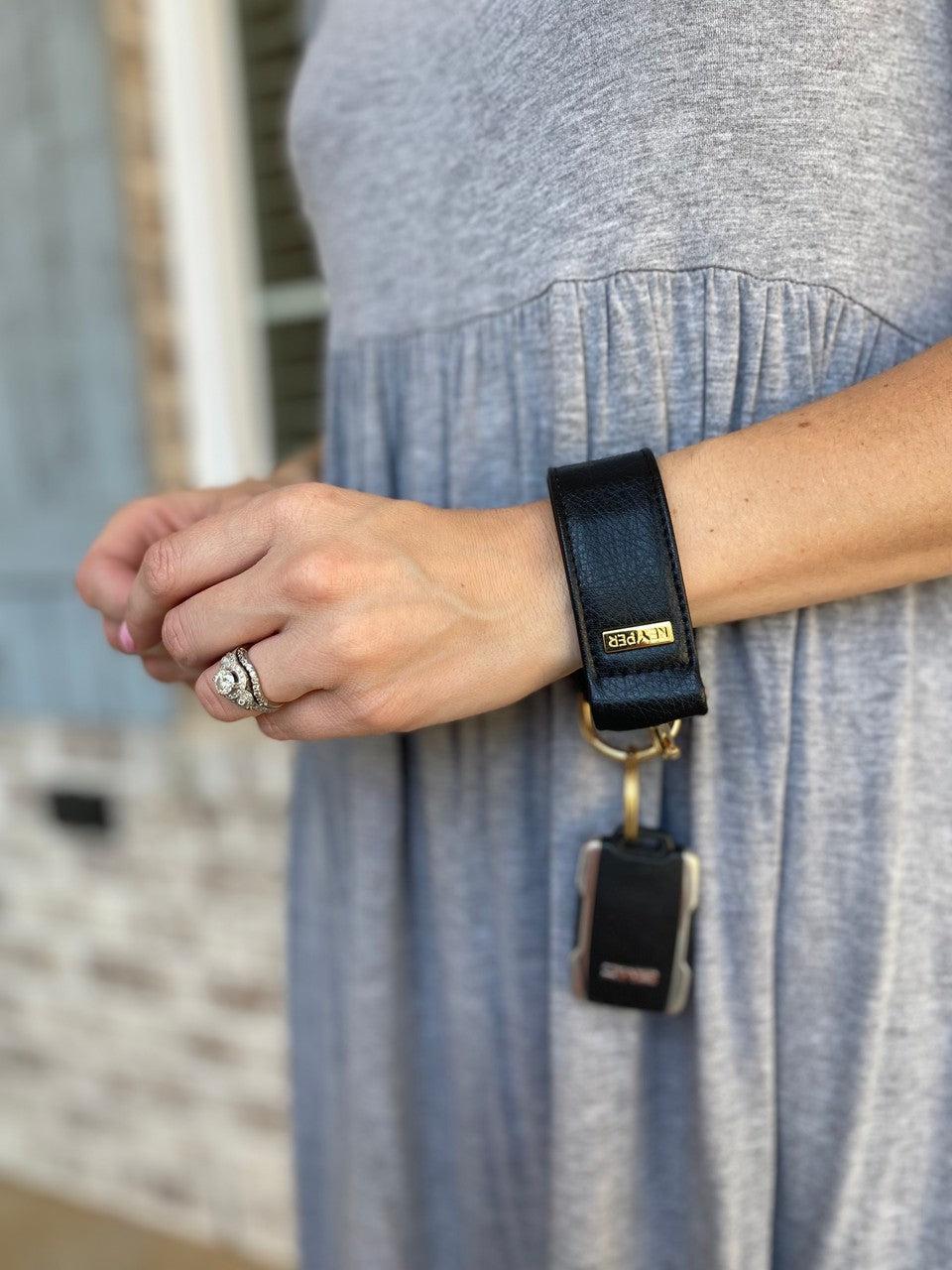 A Classic Black PREMIUM LEATHER KEYPER® key ring features a black leather bracelet with a gold clasp and branded KEYPER tag, attached to a key.