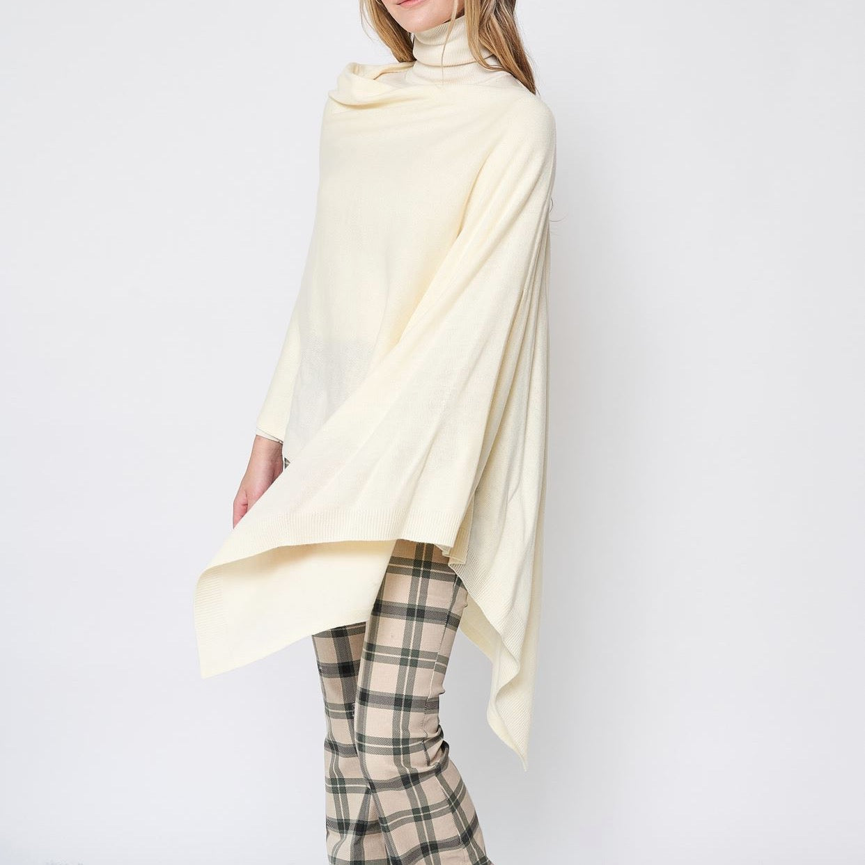 Someone wearing the Take With Me Travel Poncho by Ellison + Young with plaid pants against a plain white background.