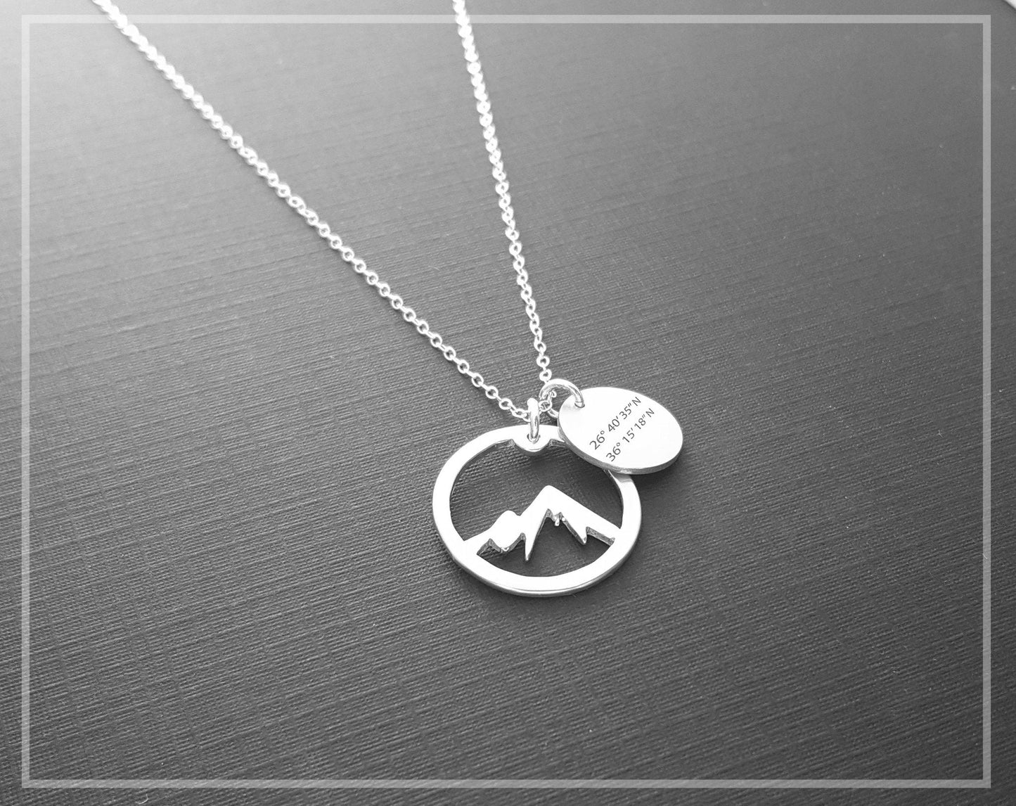 The Coordinate Mountain Necklace by Sincerely Silver is a silver piece featuring a mountain design pendant and a round one engraved with coordinates.