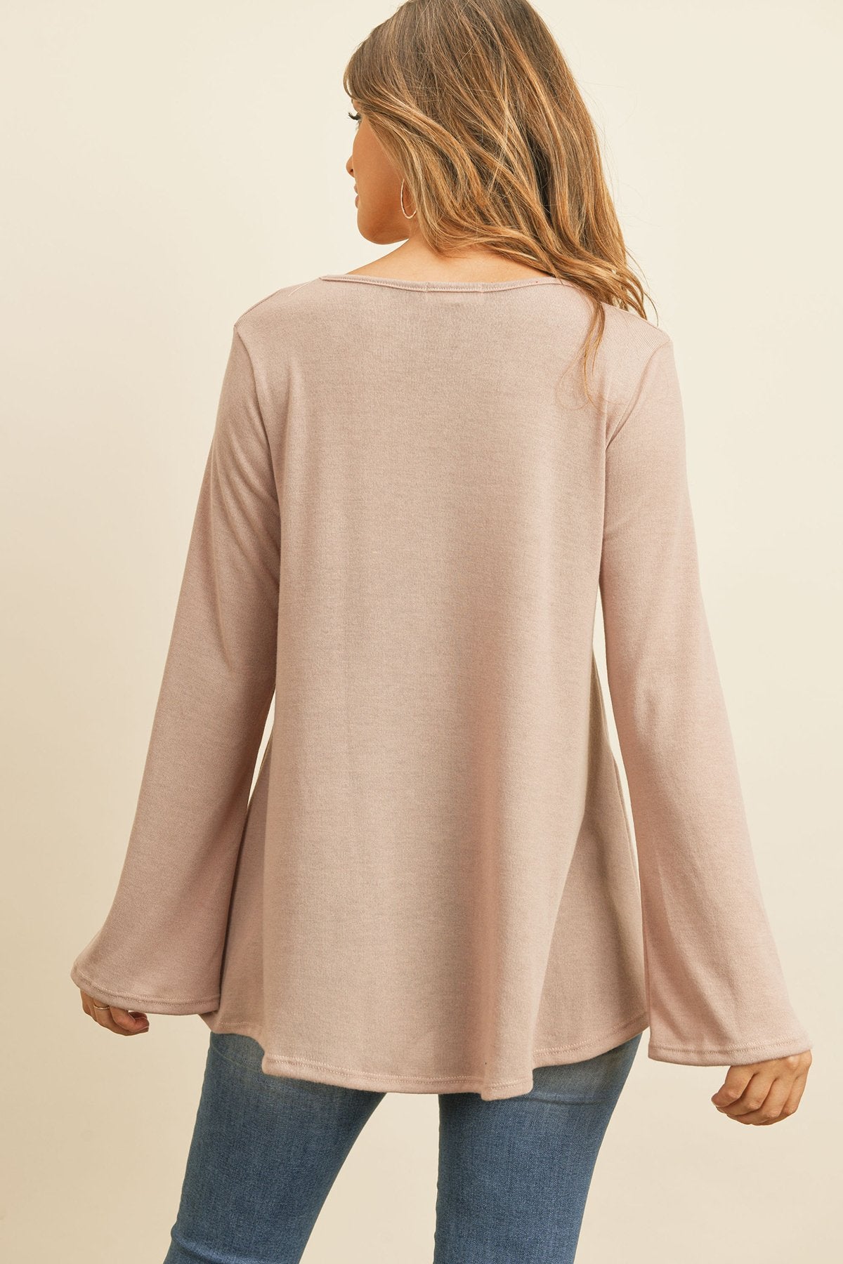 A person wearing a Riah Fashion Criss Cross Neck Long Sleeve Hacci Top in Dusty Blush and blue jeans stands against a neutral background, smiling.