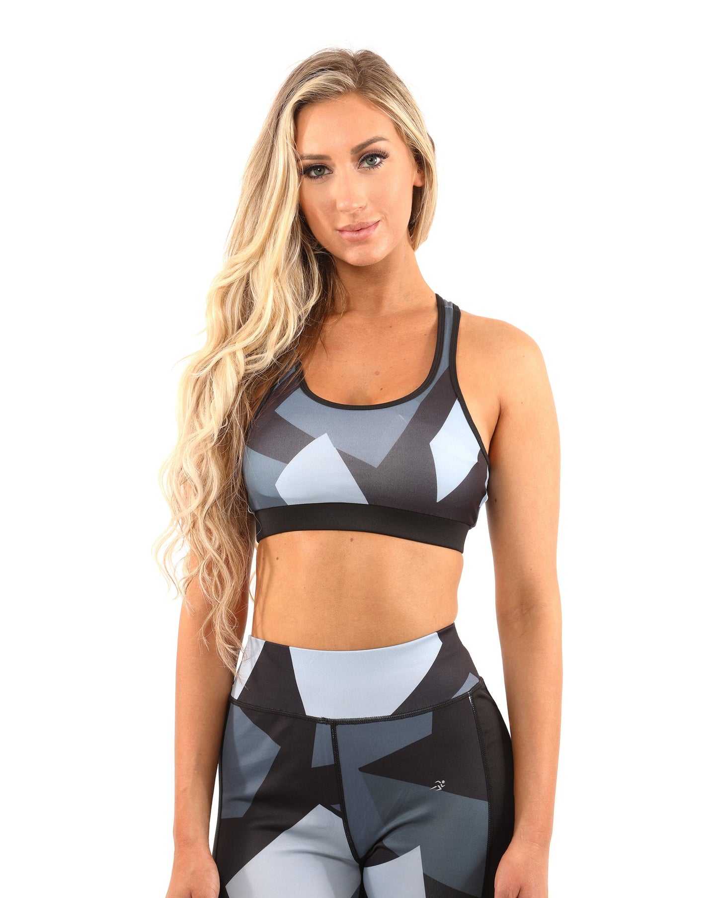 A person wearing the Savoy Active Bondi Set, consisting of geometric-patterned black and grey leggings and a sports bra, stands against a white background.