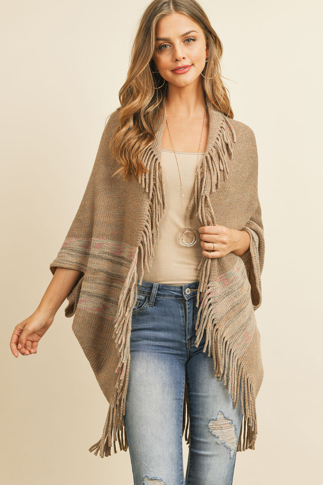 Someone is wearing a Fringe Stripe Open Front Kimono by Riah Fashion over a beige top and ripped jeans, standing against a plain background.