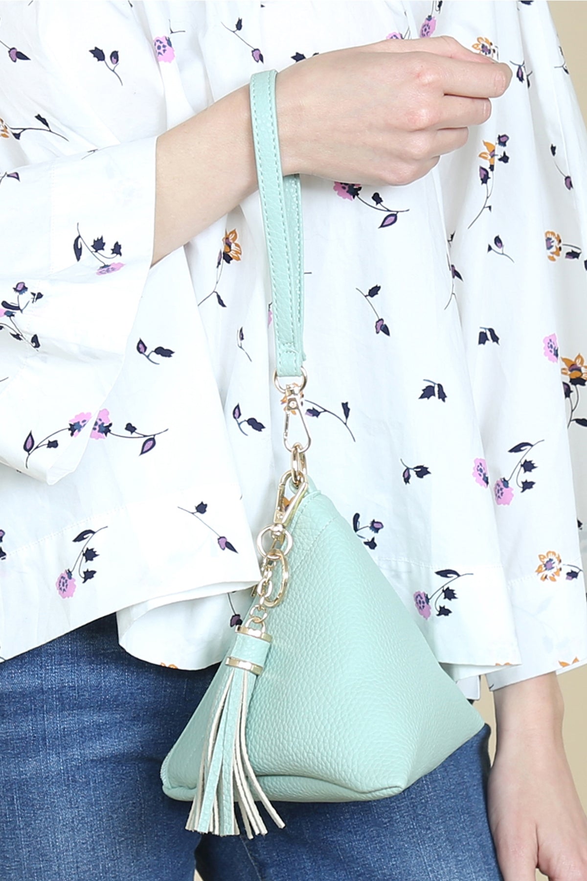A person in a white shirt and jeans is holding the Riah Fashion Pyramid Shape Tassel Wristlet Leather Bag in orange.