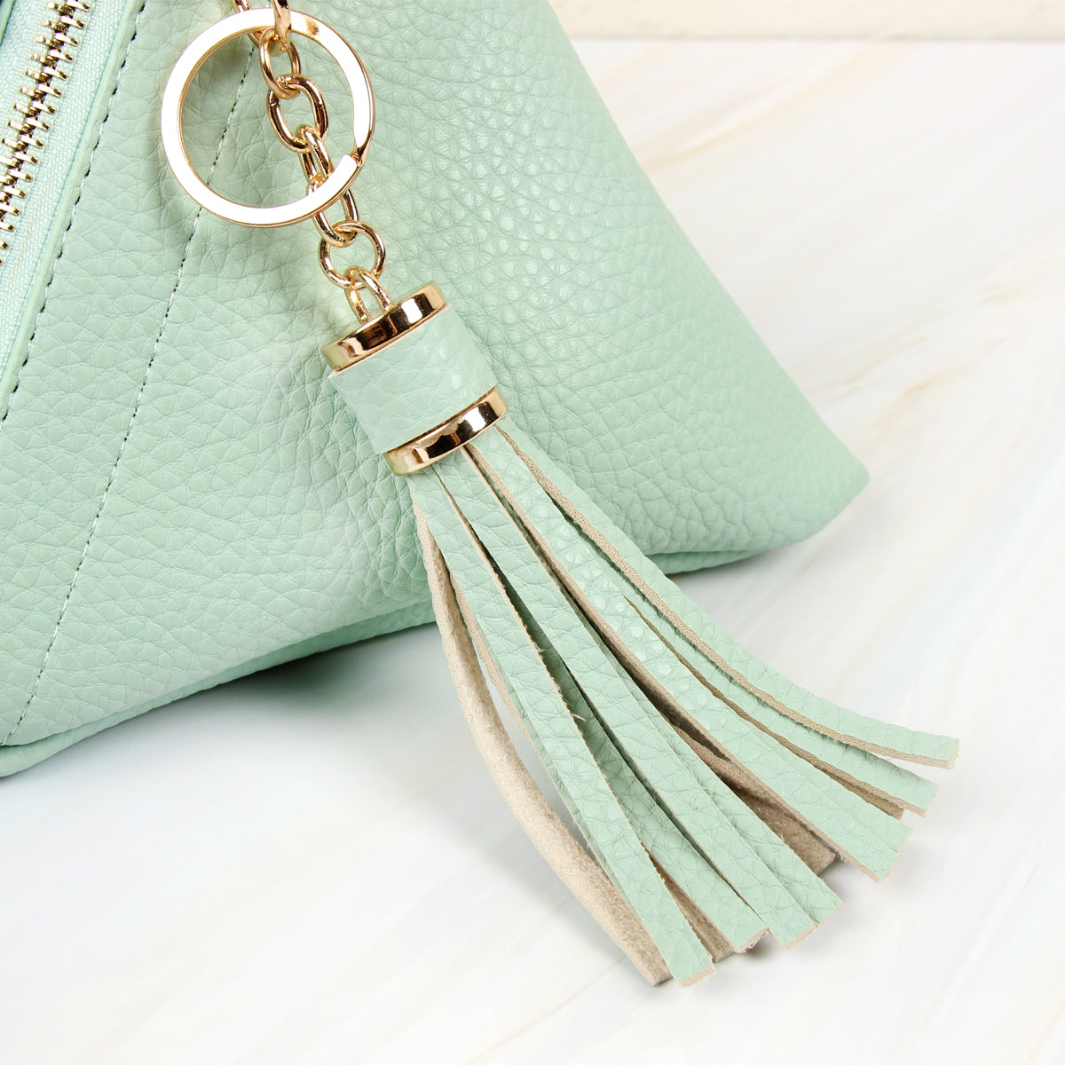 A person in a white shirt and jeans is holding the Riah Fashion Pyramid Shape Tassel Wristlet Leather Bag in orange.