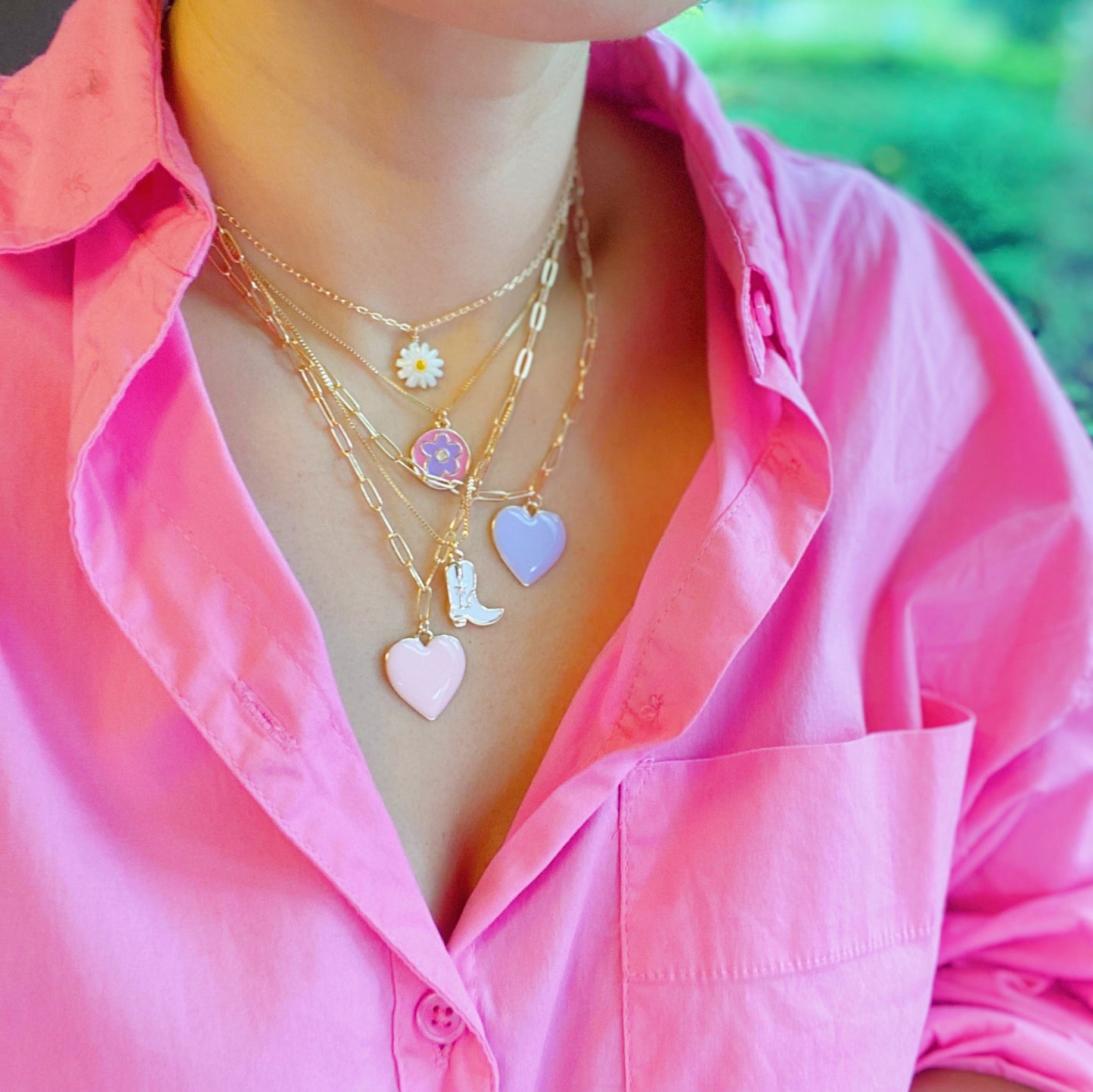 Two Cow Girl Boot Pendant Necklaces by Ellison + Young, one with a white boot and the other with a pink boot, are displayed on a marble surface.