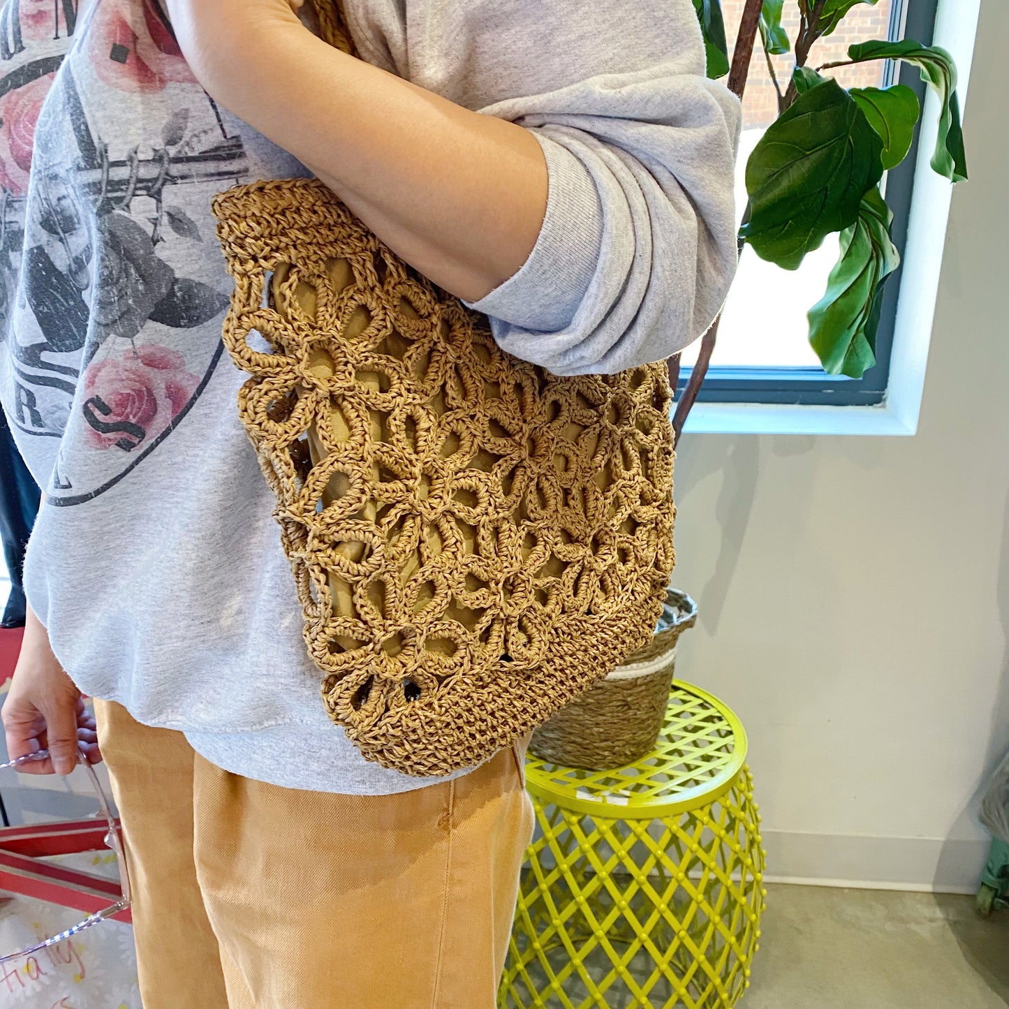 A person smiles while standing outdoors with a clear blue sky and trees in the background, wearing a yellow striped sweater and holding an Ellison + Young Hand Made Muted Floral Tote.