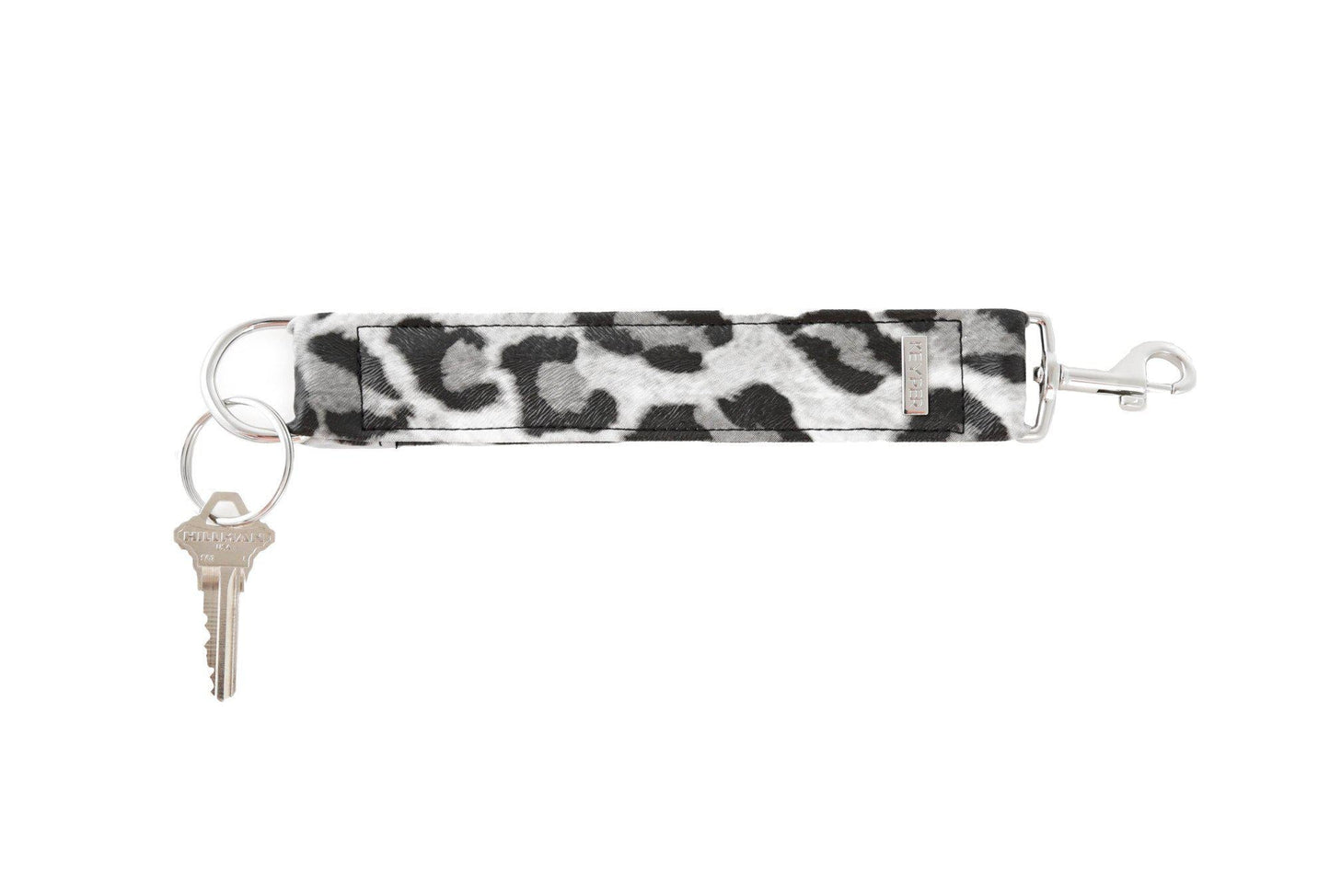 The KEYPER brands Snow Leopard Vegan Leather KEYPER® Key Ring features a leopard print design, a gold key ring with an attached key, and a small rectangular gold label.