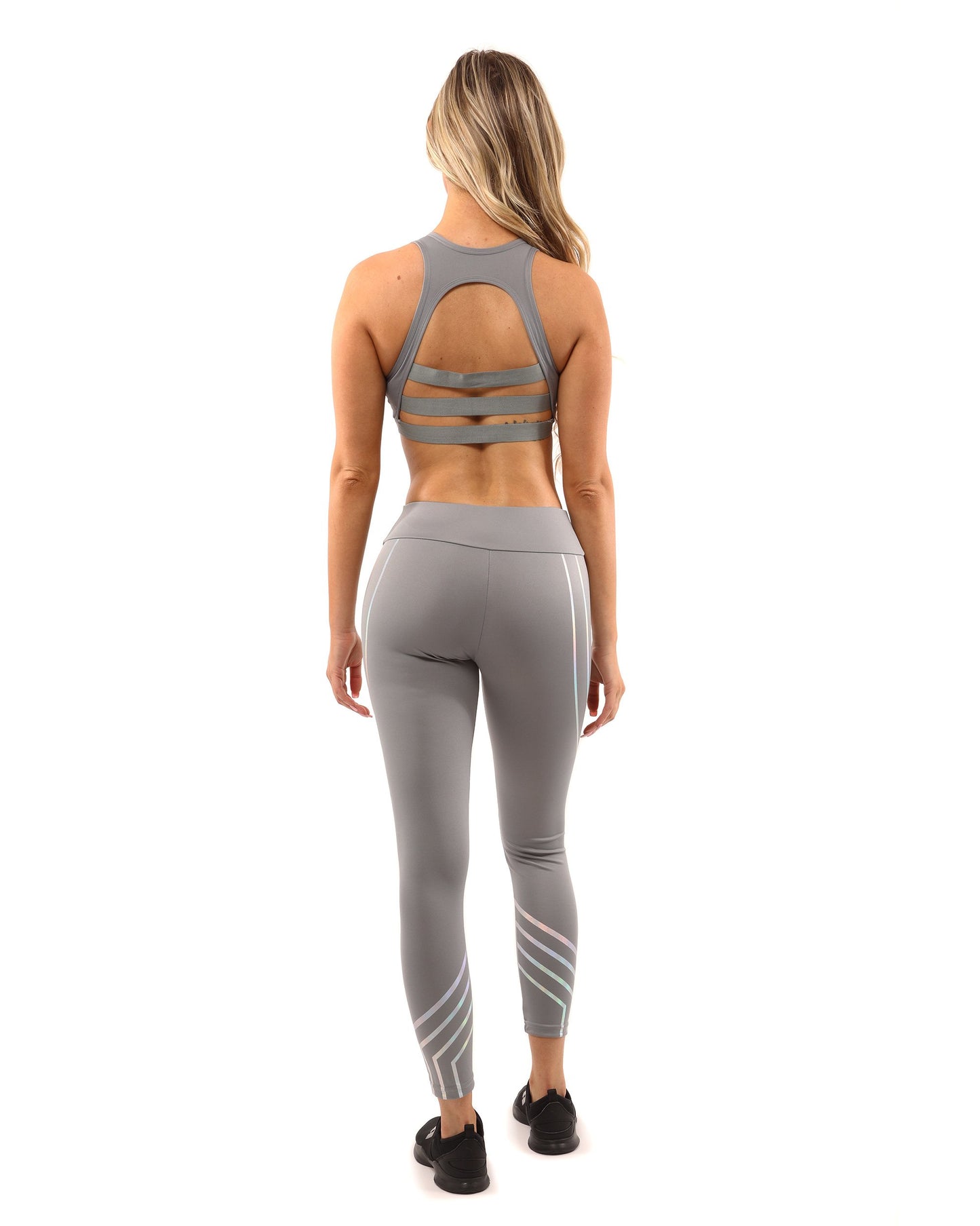 A woman in Savoy Actives grey Laguna Leggings stands on outdoor steps, adjusting her top while facing away from the camera.
