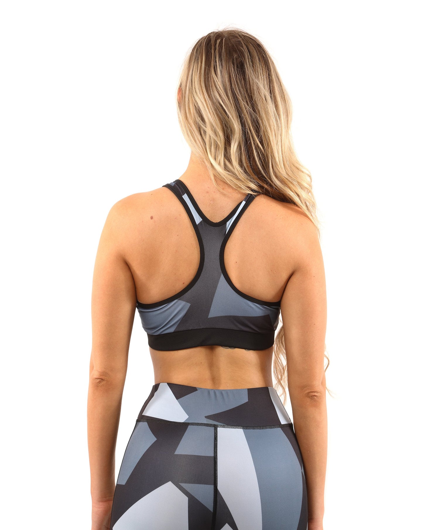 A person wearing the Savoy Active Bondi Set, consisting of geometric-patterned black and grey leggings and a sports bra, stands against a white background.