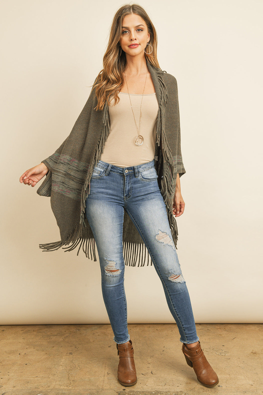 Someone is wearing a Fringe Stripe Open Front Kimono by Riah Fashion over a beige top and ripped jeans, standing against a plain background.