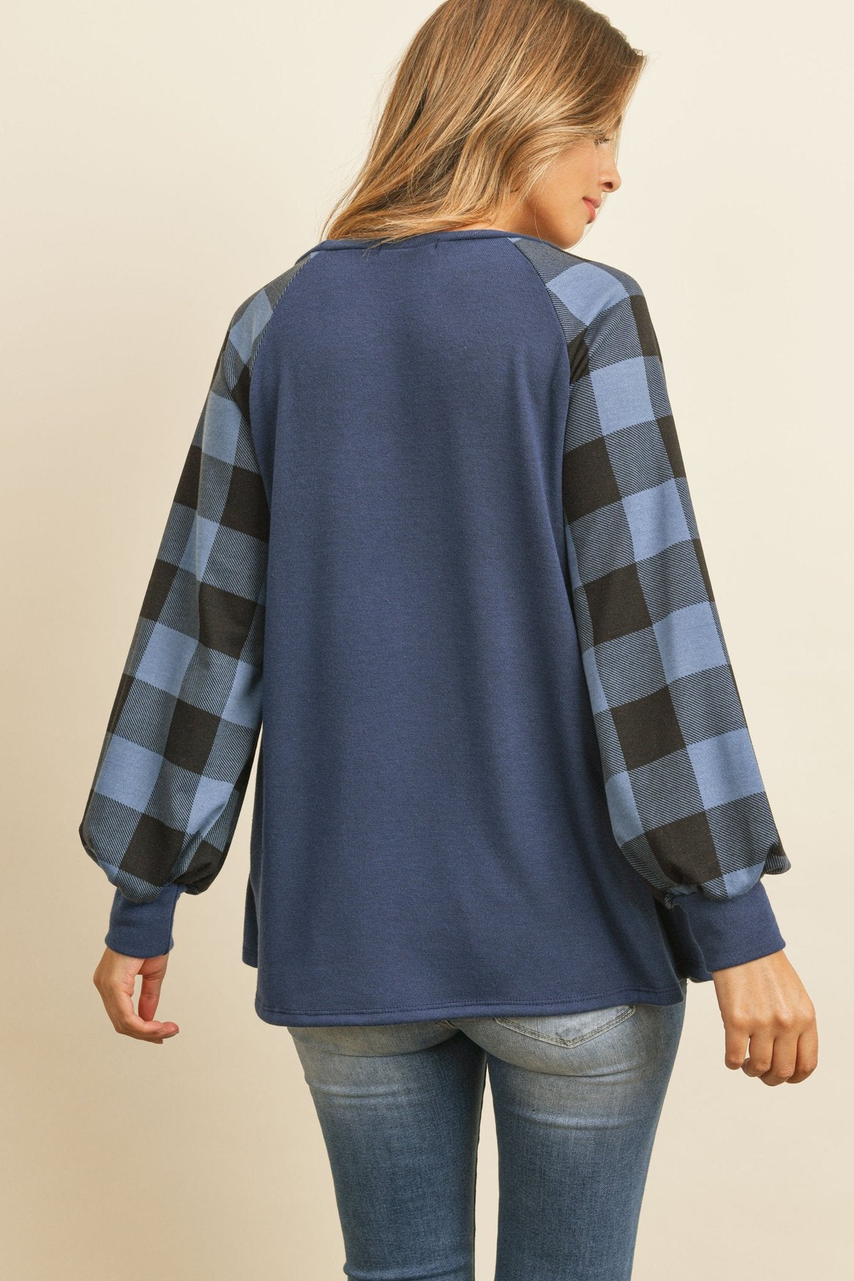 A woman wearing a faded denim plaid puff sleeved round neck top by Riah Fashion and ripped jeans stands against a plain background.