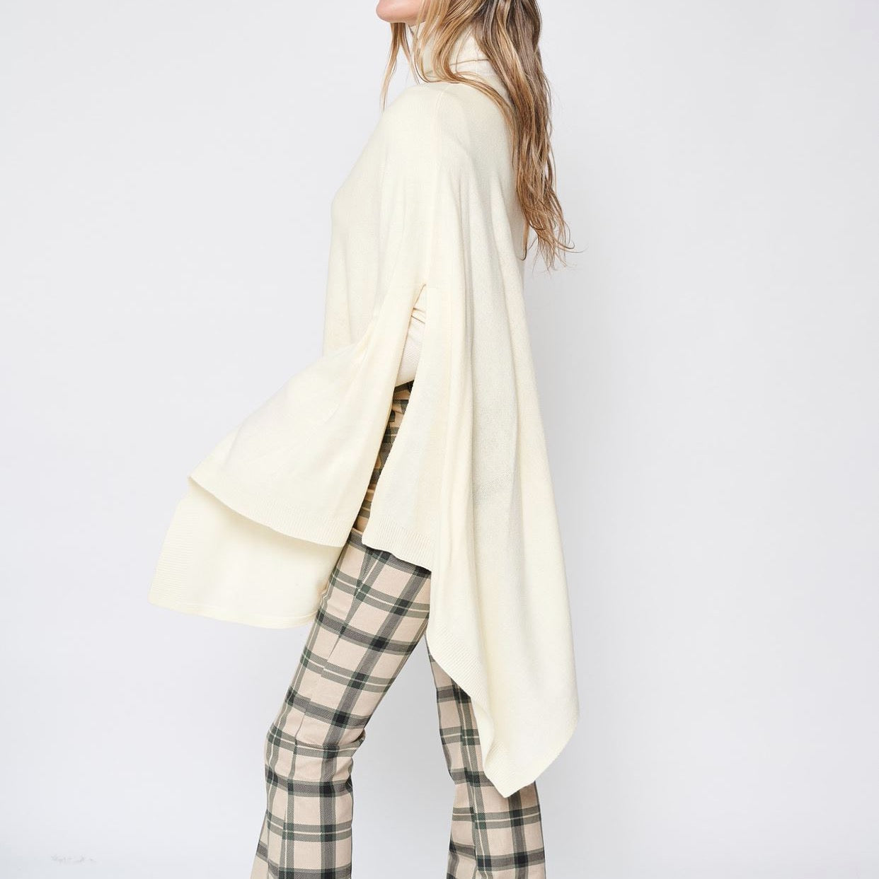 Someone wearing the Take With Me Travel Poncho by Ellison + Young with plaid pants against a plain white background.