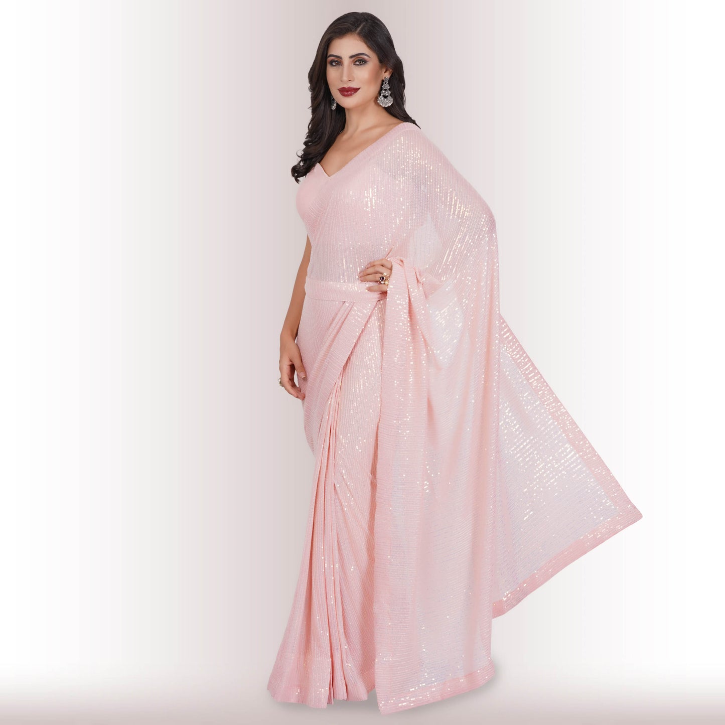 A person wearing Chiros Ready Made Sequin Saree in Blush poses with one hand on their hip against a light background.