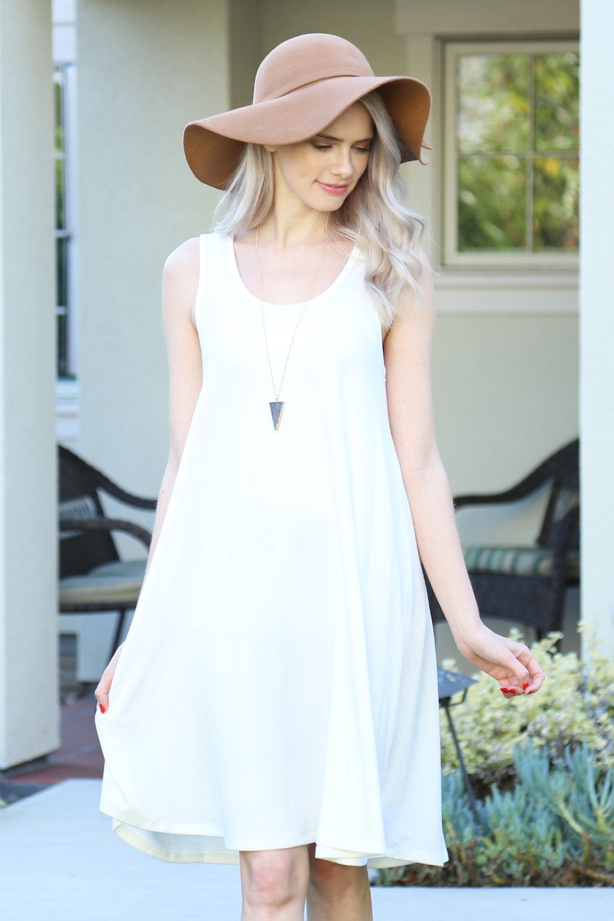 A person with long, light-colored hair wears a Sleeveless Flared Pocket Dress in light green by Riah Fashion outside, holding the dresss sides along with a triangular pendant necklace.