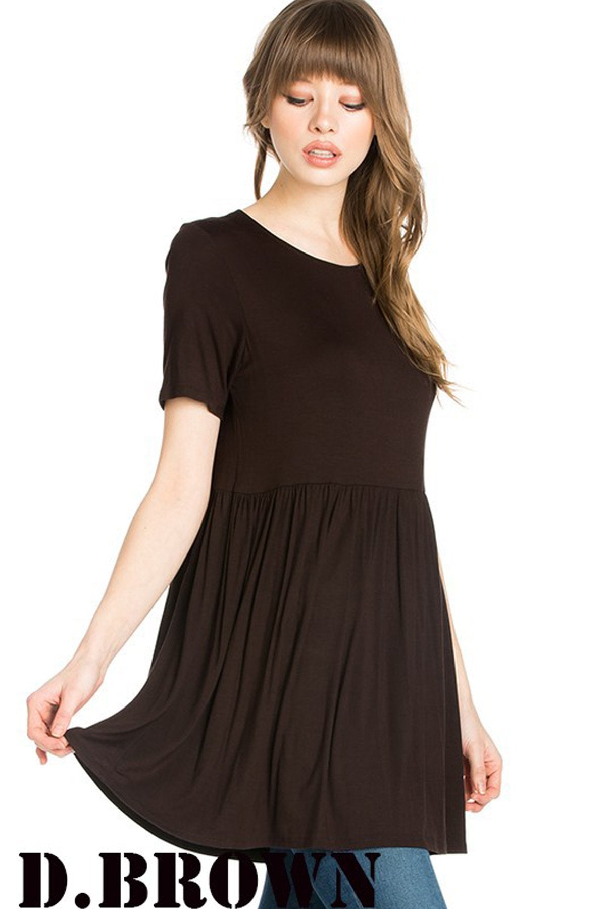 A woman stands outdoors wearing a beige Riah Fashion Short Sleeve Empire Waist Tunic paired with a long necklace.