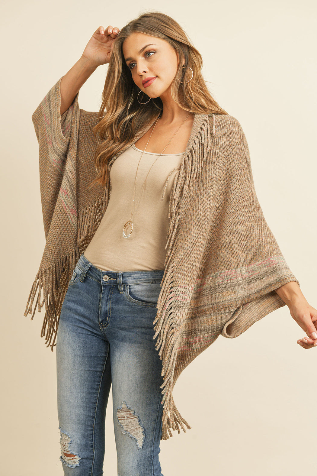 Someone is wearing a Fringe Stripe Open Front Kimono by Riah Fashion over a beige top and ripped jeans, standing against a plain background.