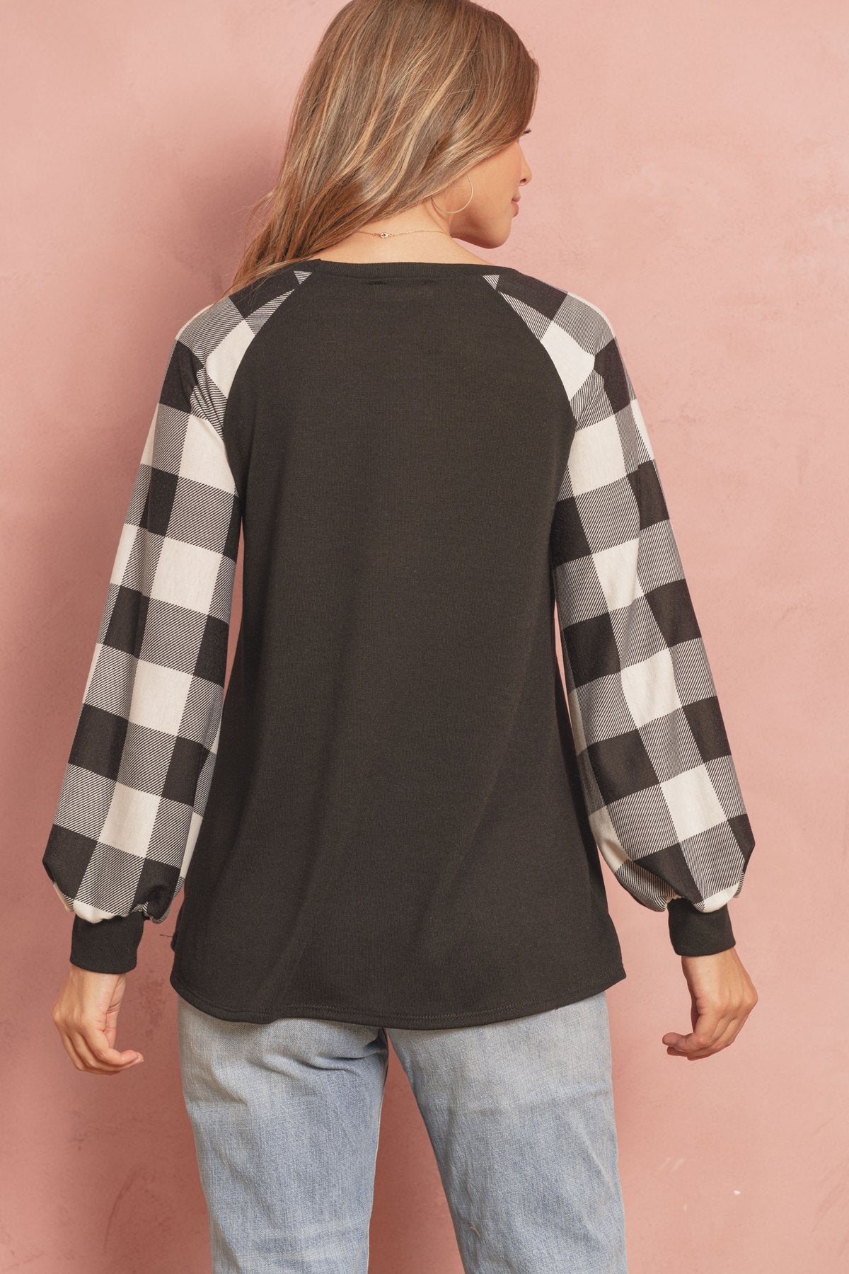 A woman wearing a faded denim plaid puff sleeved round neck top by Riah Fashion and ripped jeans stands against a plain background.
