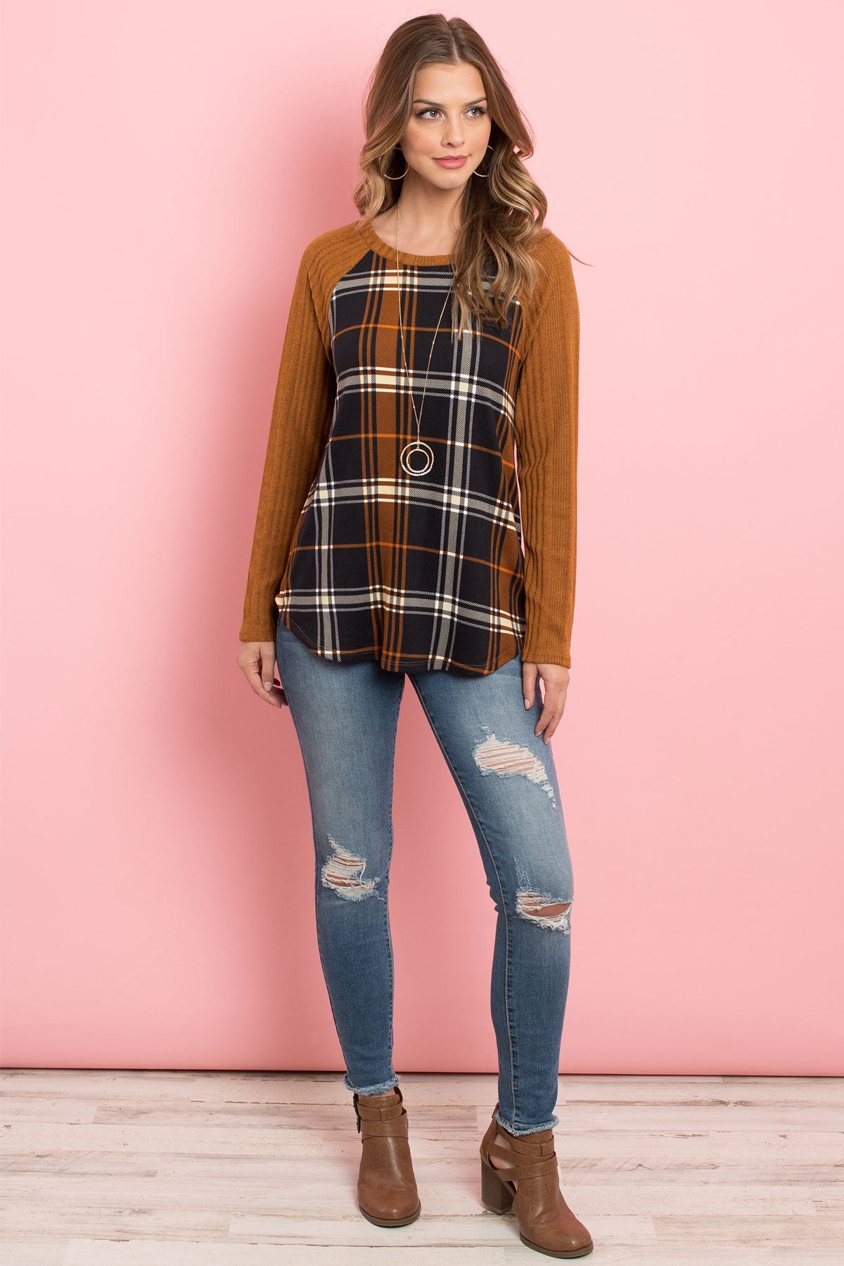 A person wearing a Riah Fashion Long Sleeve Knit Detail Contrast Plaid Top and jeans stands against a pink background, smiling.