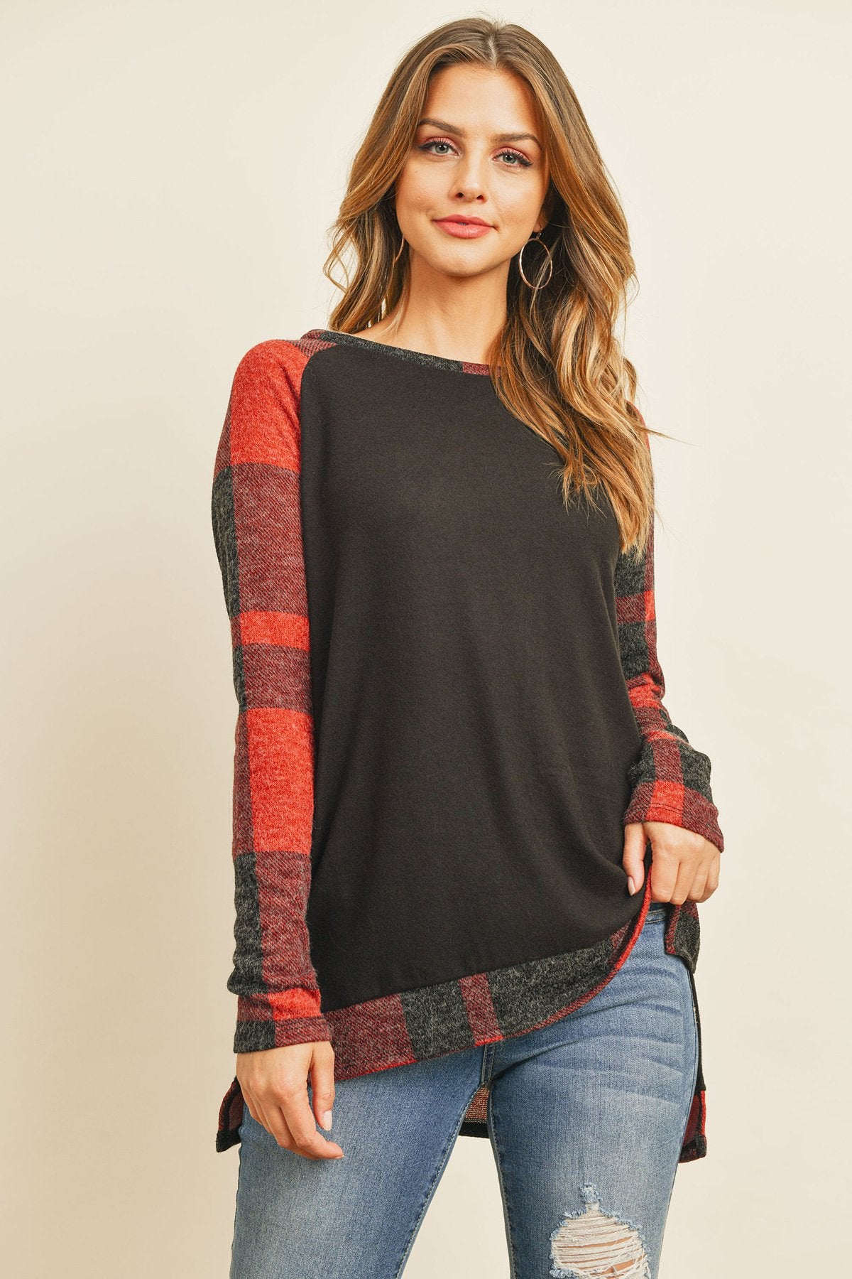 A woman in a Riah Fashion Brush Hacci Plaid Contrast Long Back Hem Top with red and beige accents, paired with blue ripped jeans, stands against a plain background.