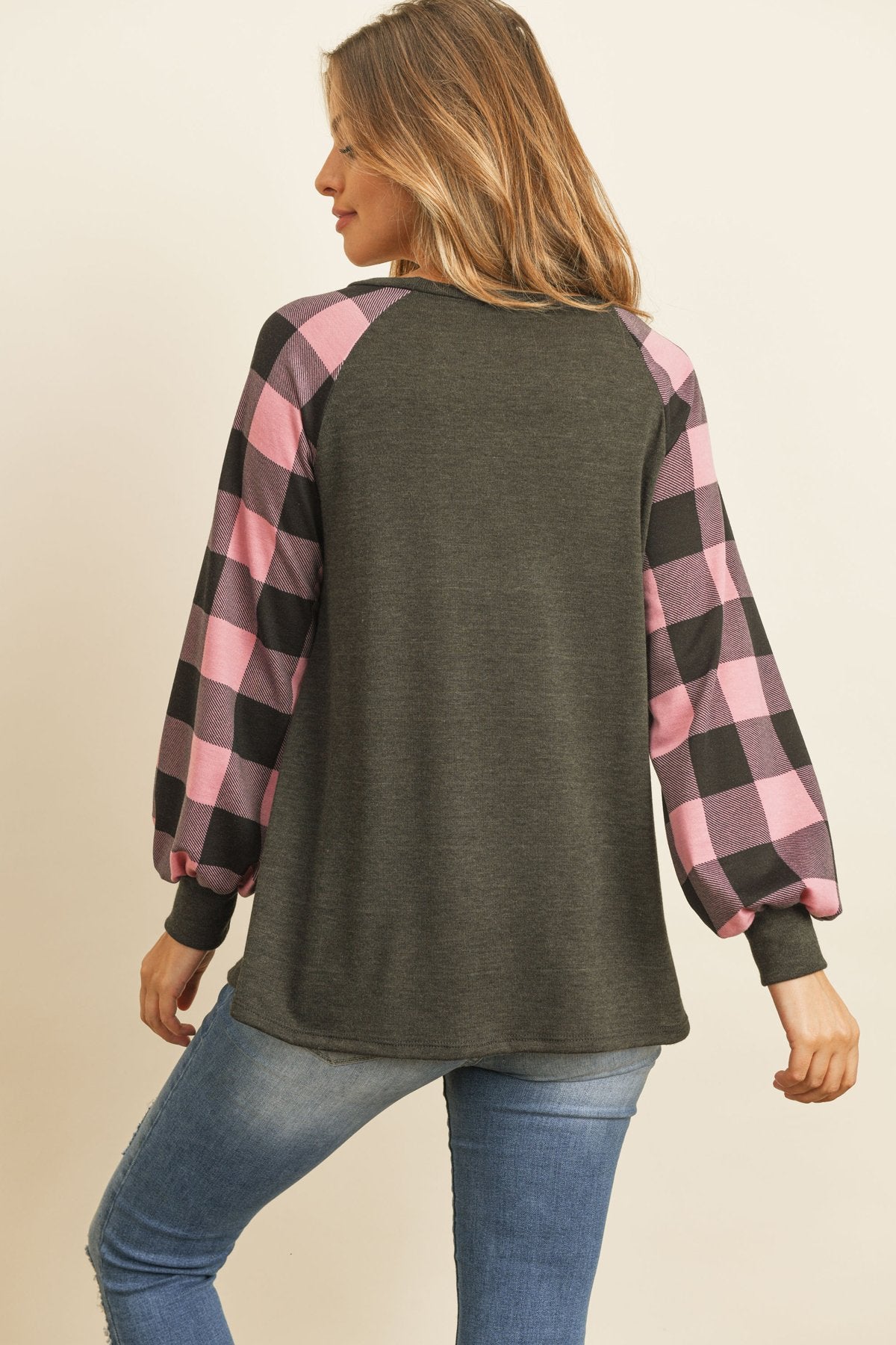 A woman wearing a faded denim plaid puff sleeved round neck top by Riah Fashion and ripped jeans stands against a plain background.