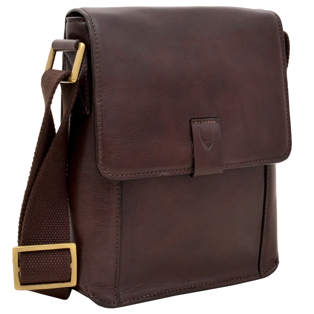 The Aiden Genuine Leather Mini Crossbody by Hidesign is a brown leather shoulder bag featuring a flap cover and an adjustable fabric strap with a brass buckle.