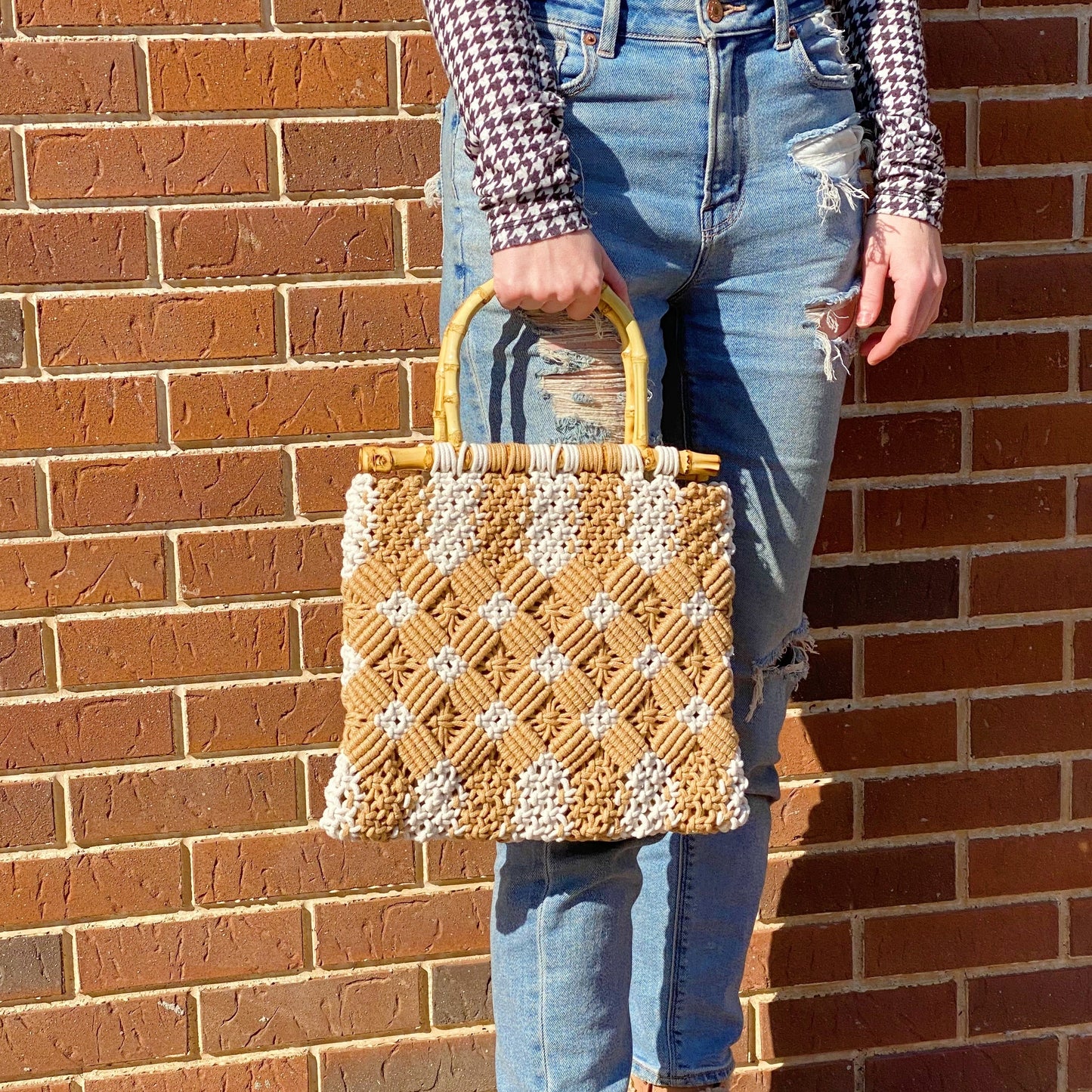A person holds the Ellison + Young Bamboo Babe Tote, wearing a houndstooth shirt and ripped jeans. The background features a paved walkway and street.