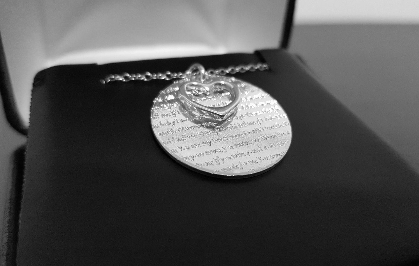 The Words of Love Necklace by Sincerely Silver is a silver piece with a round pendant showcasing printed text and an overlapping heart-shaped cutout.