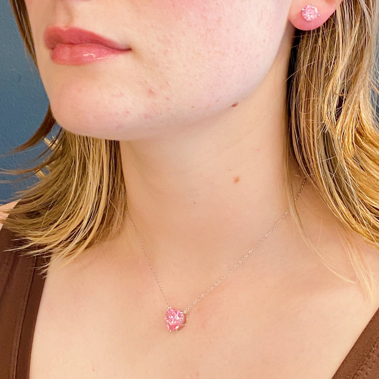 Two Absolute Beauty sterling silver heart necklaces by Ellison + Young; one with a pink gem, the other with a clear gem, against a white background.