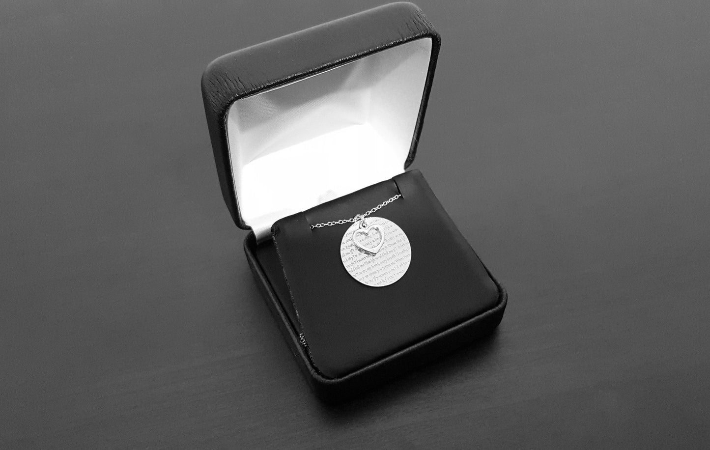 The Words of Love Necklace by Sincerely Silver is a silver piece with a round pendant showcasing printed text and an overlapping heart-shaped cutout.