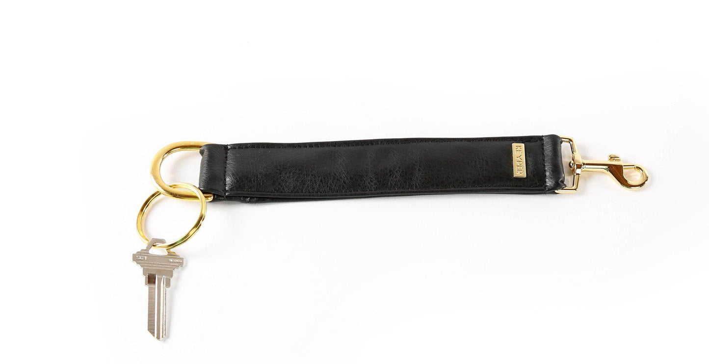 The Classic Black Vegan Leather KEYPER® Key Ring by KEYPER features a black leather wristband with a gold keyring that holds two keys.