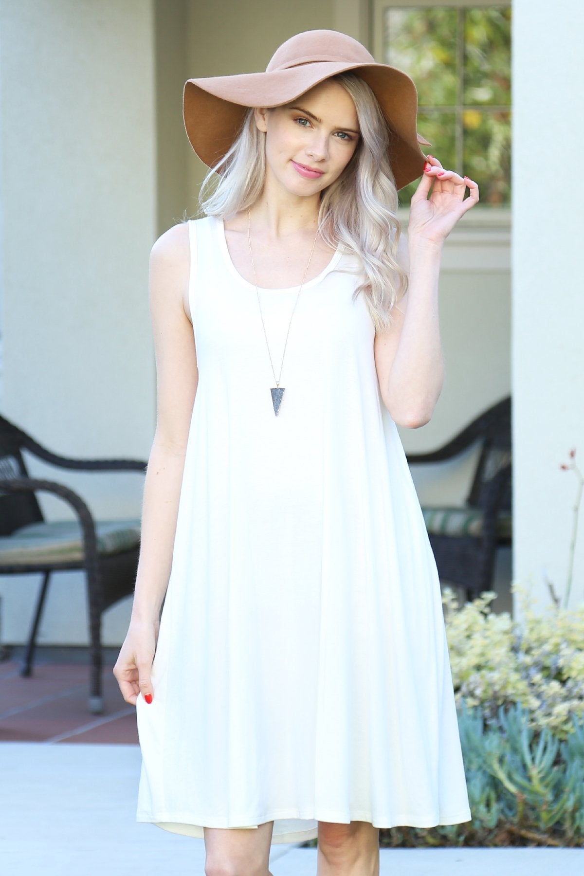 A person with long, light-colored hair wears a Sleeveless Flared Pocket Dress in light green by Riah Fashion outside, holding the dresss sides along with a triangular pendant necklace.