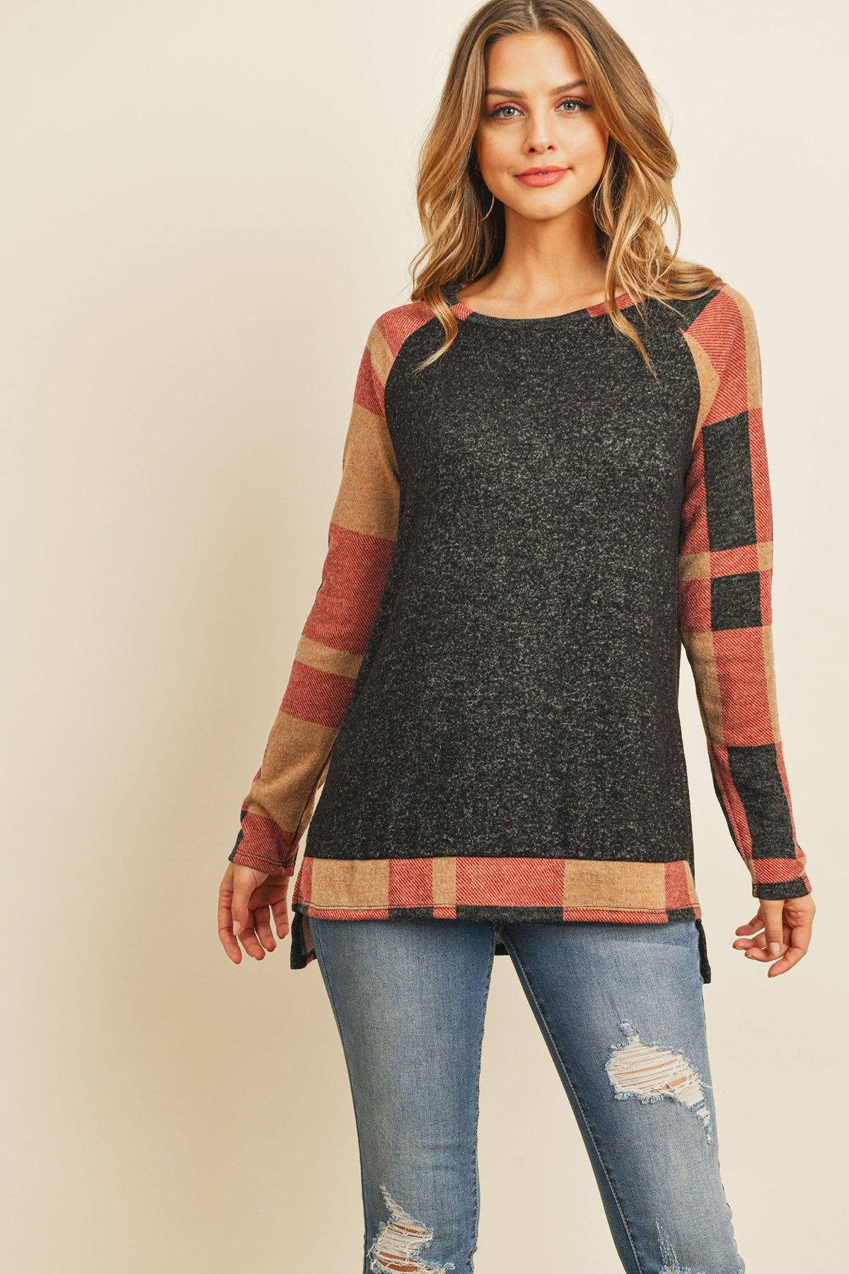 A woman in a Riah Fashion Brush Hacci Plaid Contrast Long Back Hem Top with red and beige accents, paired with blue ripped jeans, stands against a plain background.