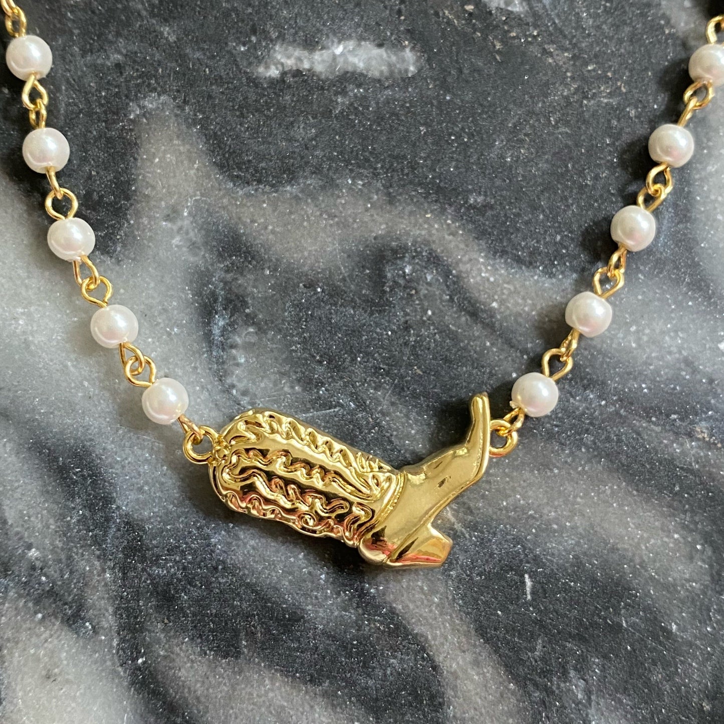 Ellison + Youngs Cowgirl Boot Pearl Chain Necklace is displayed on a marble surface.